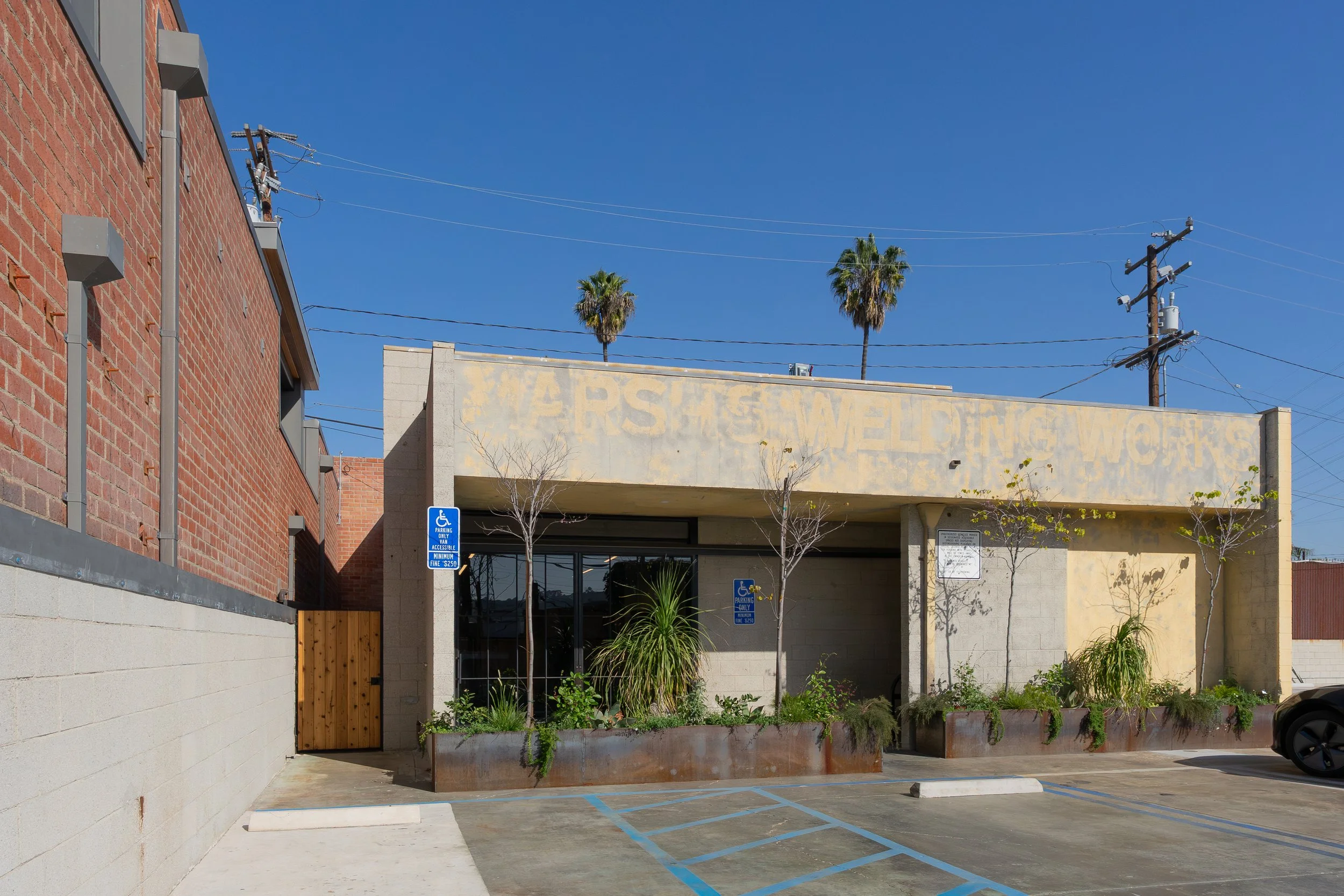 A building with a faded sign that reads 'WARS' on the front, surrounded by a parking lot with designated handicapped parking spots, small trees, and plants in planters.