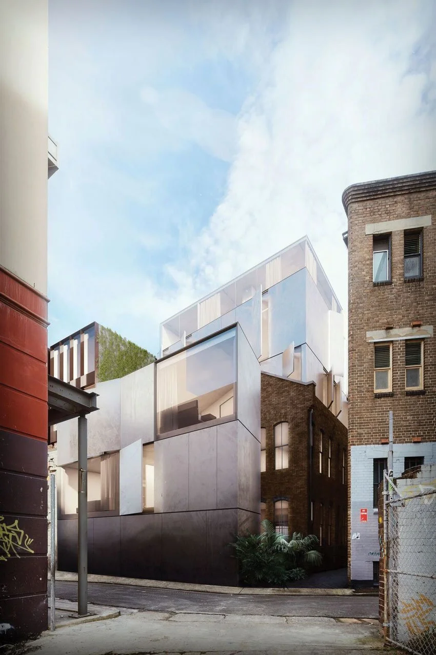 Modern multi-level building with angular design, large glass windows, and mixed materials, surrounded by older brick buildings and an alleyway.