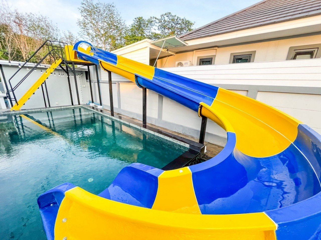 Colorful yellow and blue water slide next to a swimming pool outside a house.