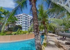 Swimming pool surrounded by palm trees and modern buildings in a tropical setting.