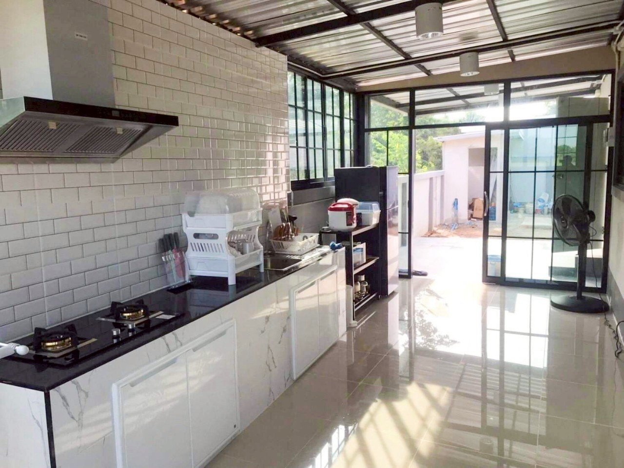 Modern kitchen with white cabinets, black countertop, gas stove, dish rack, and an open sliding glass door leading to an outdoor area.