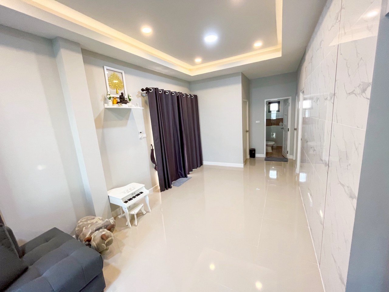 Empty living room with white walls, glossy tiled floor, closed dark curtain, and a glimpse of a bathroom with a window in the background.