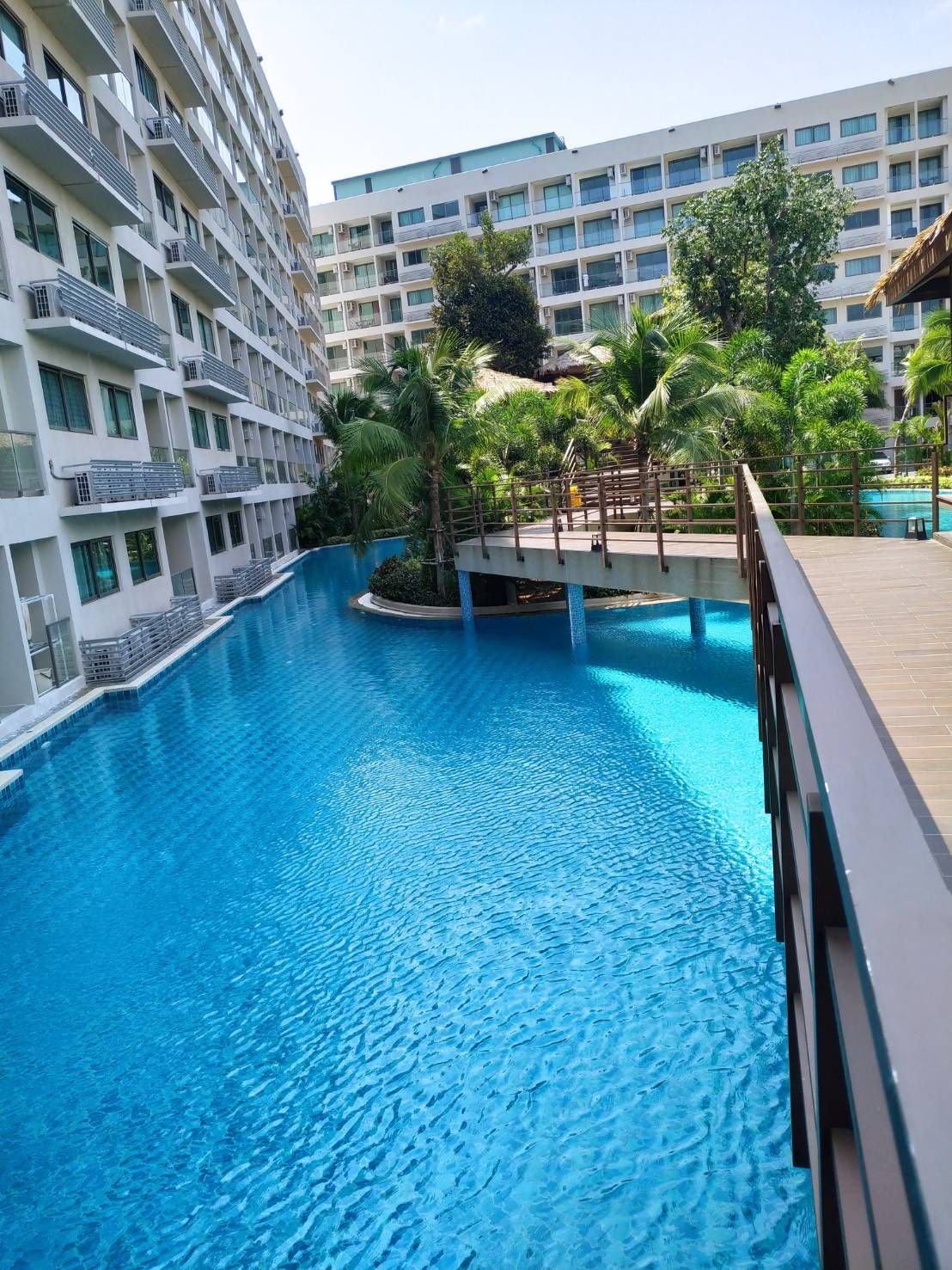 An outdoor swimming pool area surrounded by tall white apartment buildings and lush green trees.