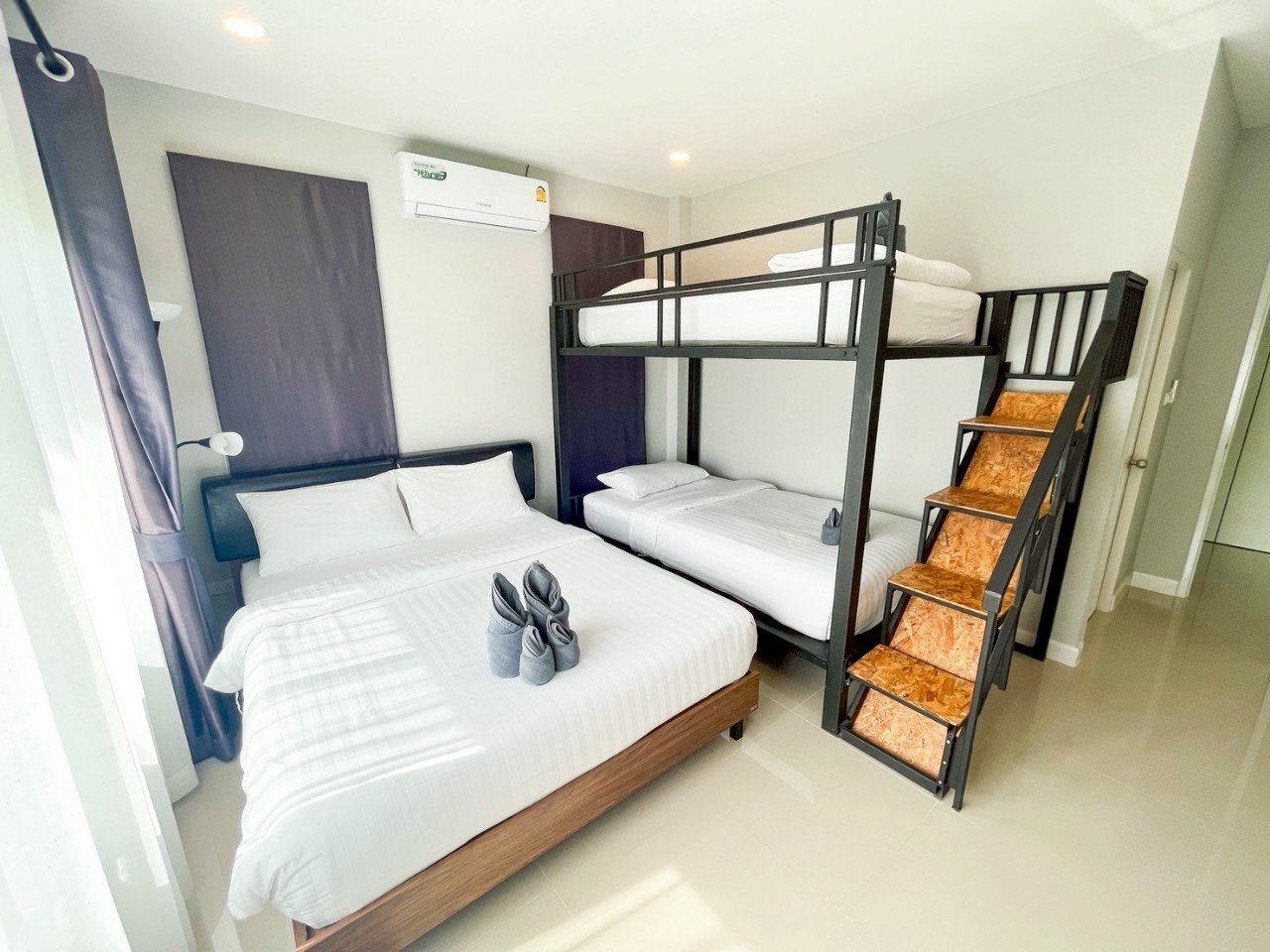 Hotel room with a double bed, bunk beds, and stairs, featuring white linens and neatly folded towels on the bed.