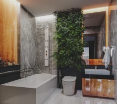 Modern bathroom with a bathtub, a toilet, a sink, and a large mirror, accented by a green plant and wooden cabinetry.