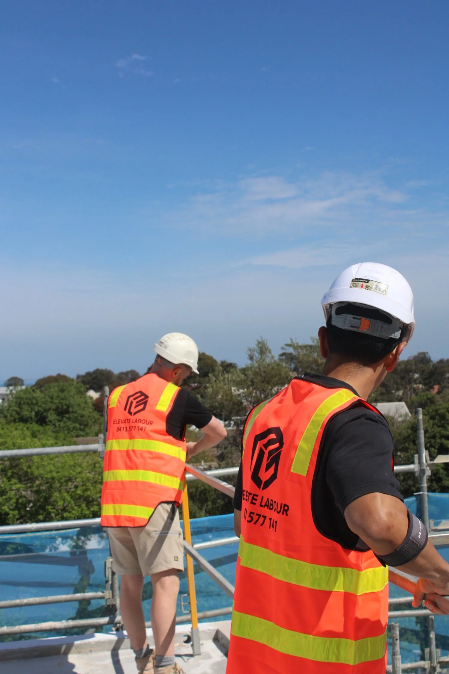Two labourers wearing hi-vis vests and hard hats working with railing on a construction site
