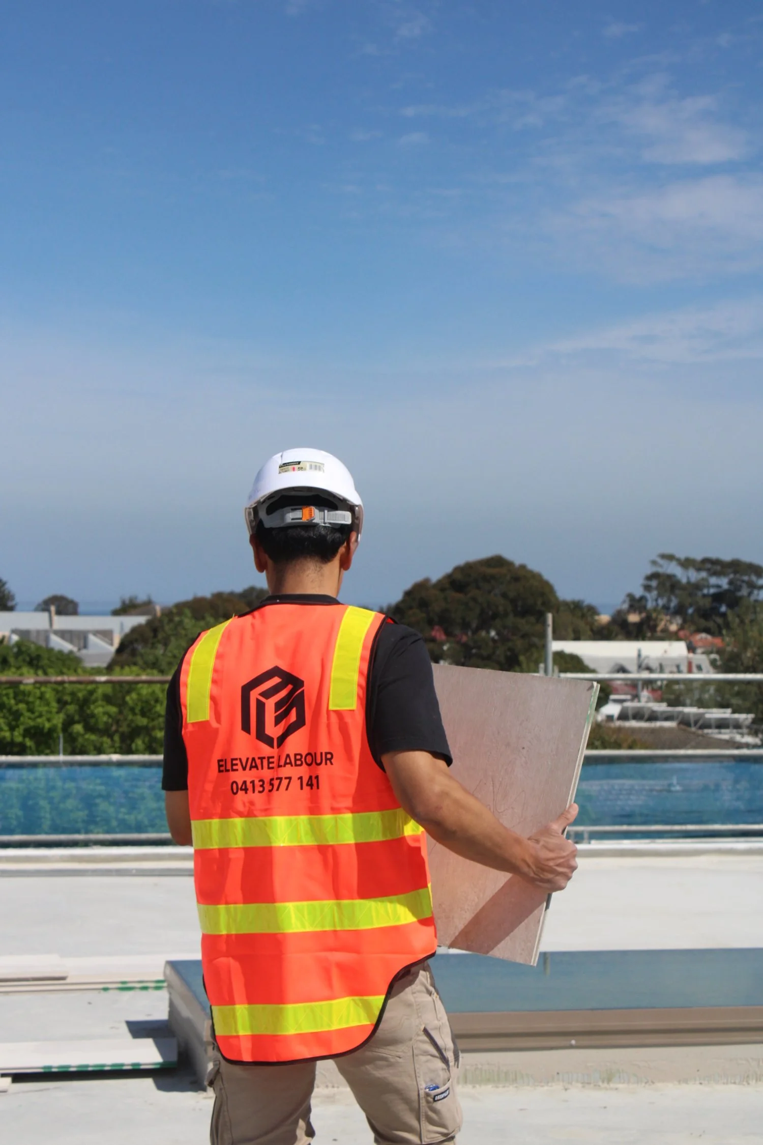 Labourer wearing hi-vis vest and hard hat moving construction materials on a commercial construction site