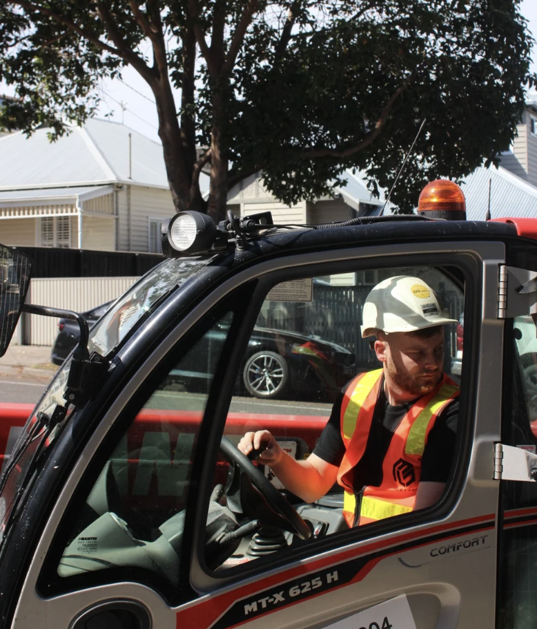Experienced worker operating heavy machinery on a Melbourne street project, equipped with hi-vis and hard hat for safe construction operations.