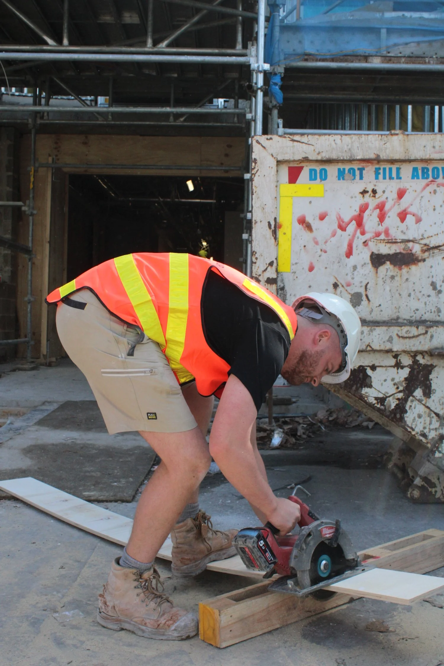 Labourer in hi-vis vest and hard hat using a circular saw on a construction site