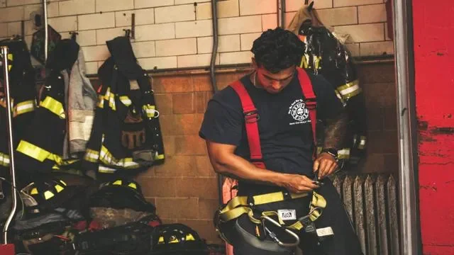 Firefighter in uniform in a fire station locker room, organizing gear on a hook or shelf.