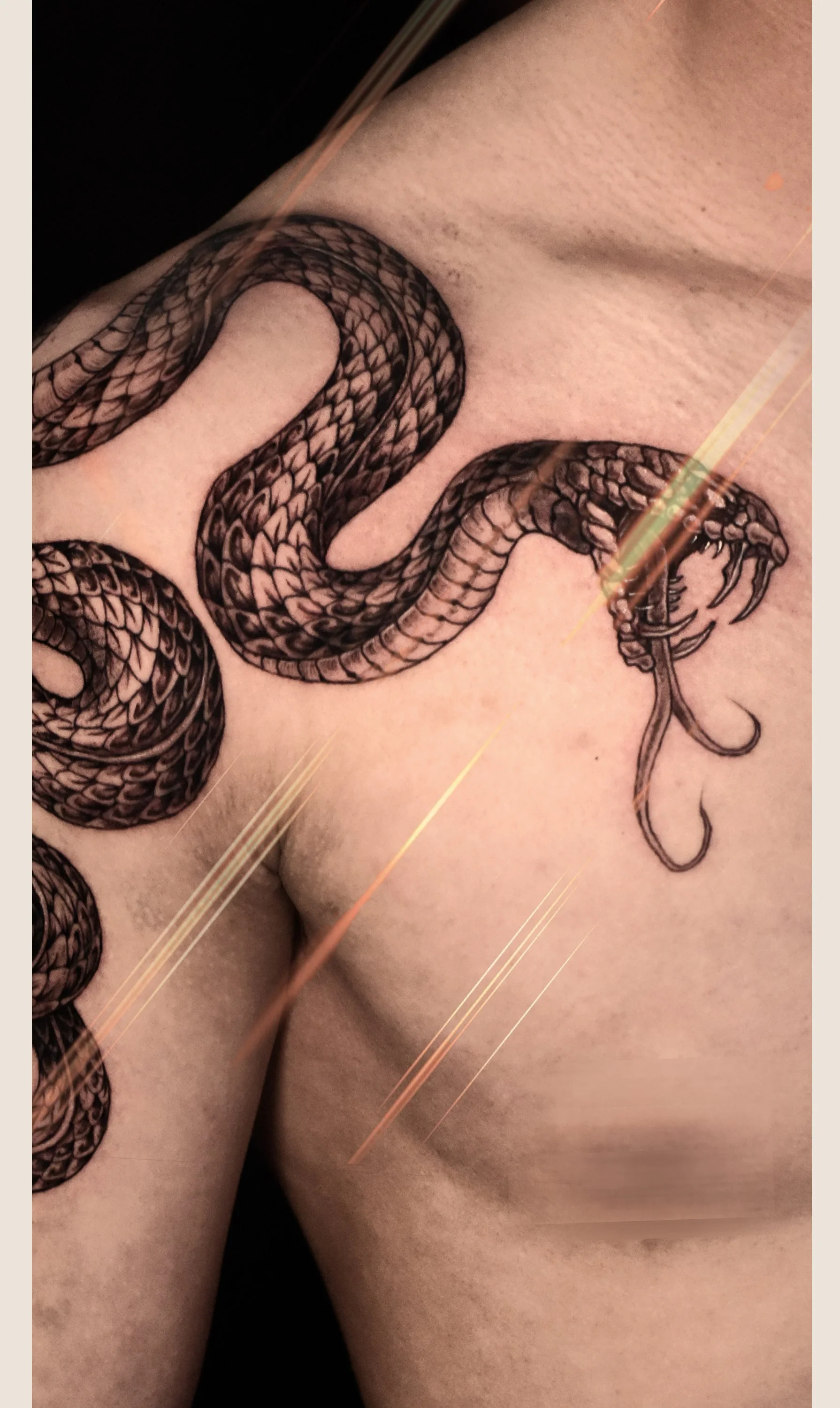 Tattoo of a black snake with detailed scales and an open mouth holding a fishing hook, located on a person's chest and shoulder area.