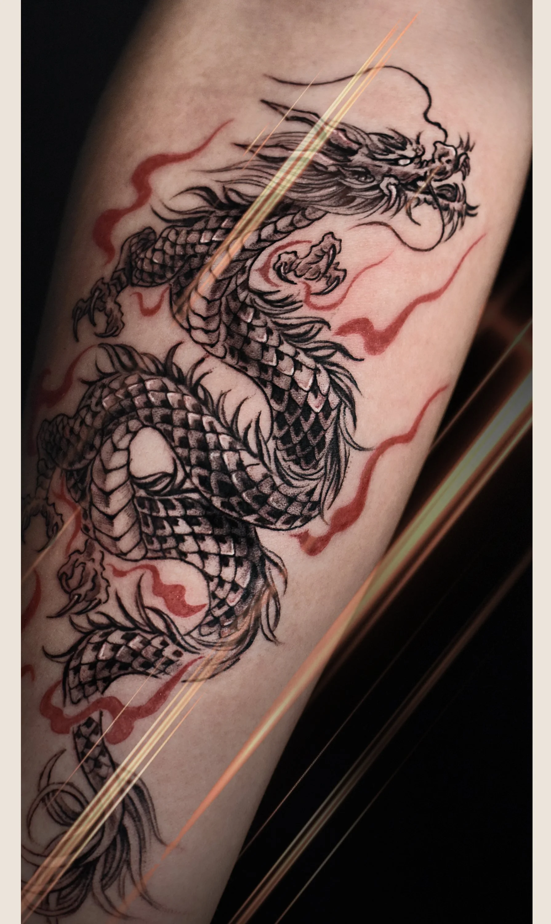 Tattoo of a detailed black and gray Chinese dragon with red accents on a person's arm.