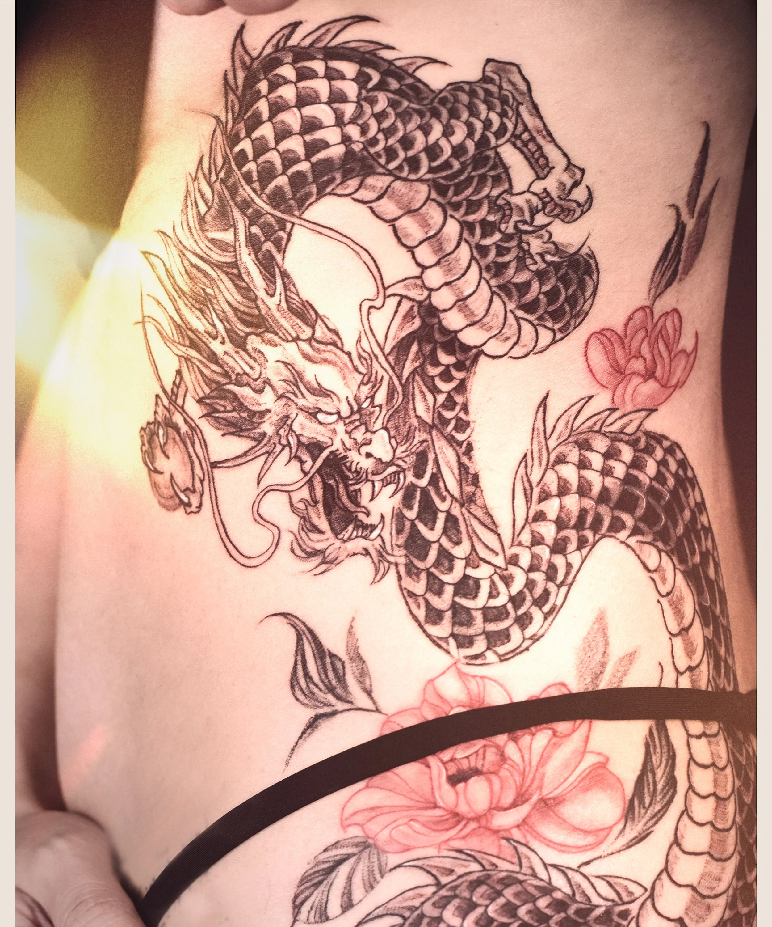 Dragon tattoo in black and red peony tattoo on side rib , craft and designed by Bored ink club, located in Los Angeles
