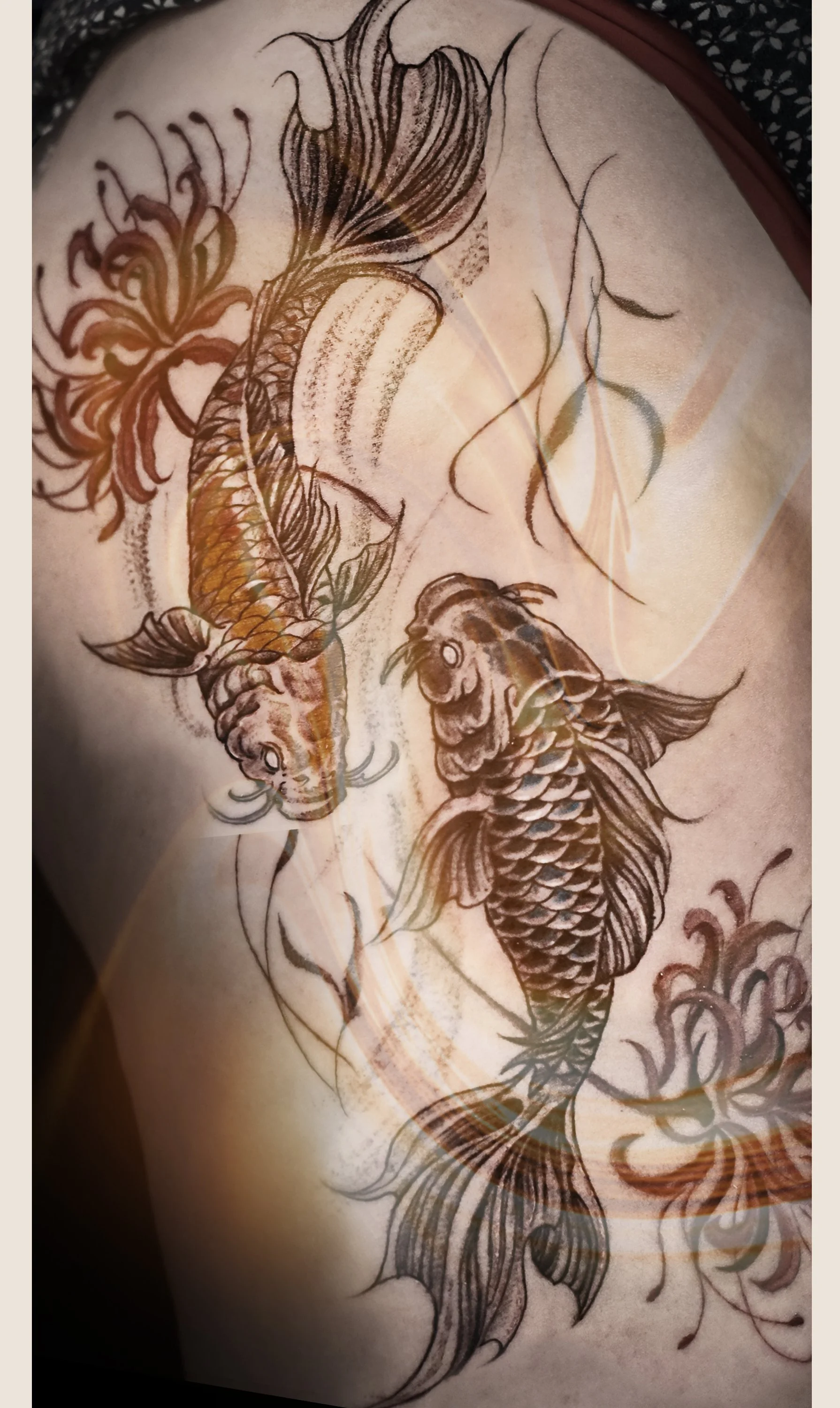 Tattoo of two koi fish swimming among water lilies on a person's skin.