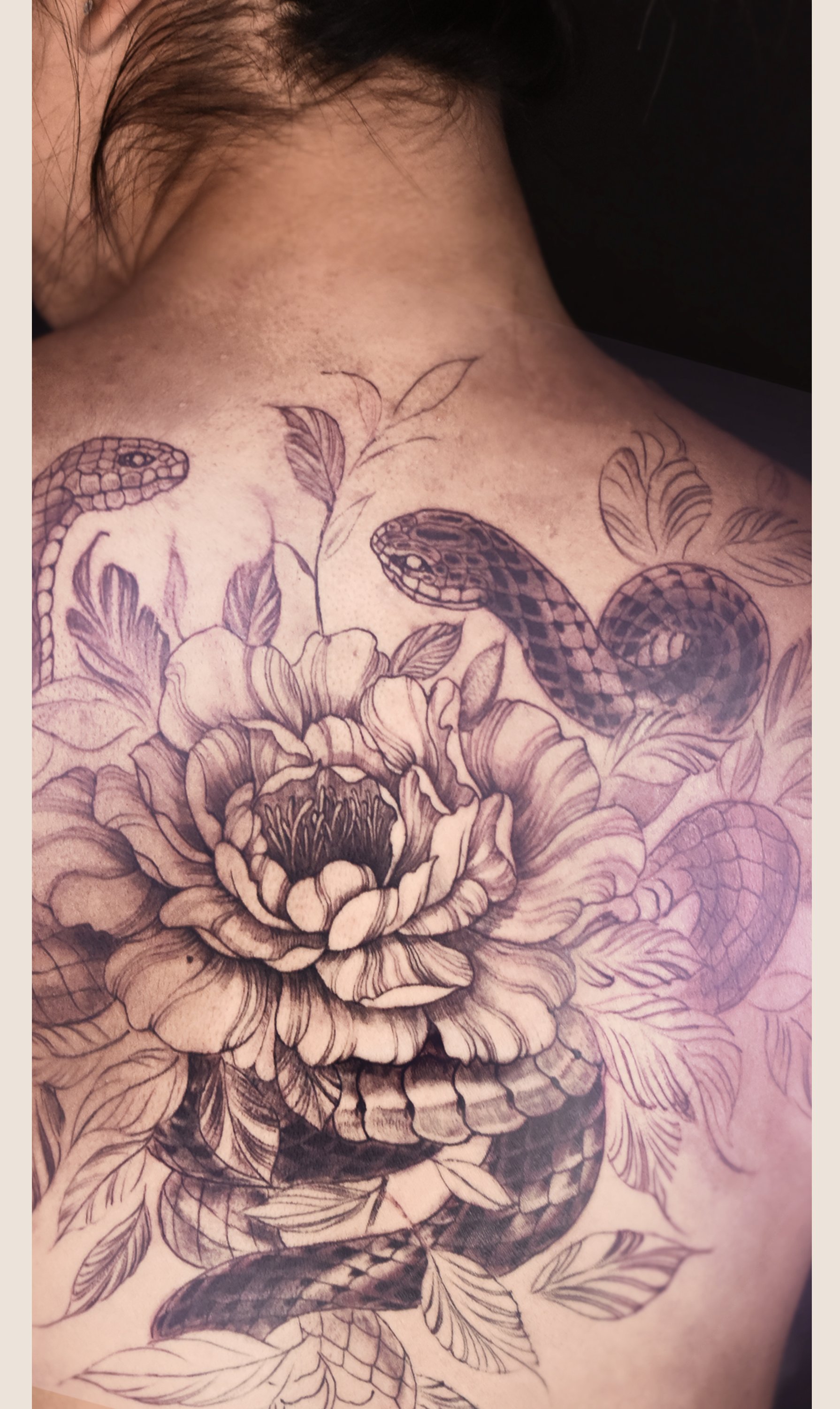 Black and gray tattoo of a snake intertwined with a large flower and leaves on a person's chest and shoulder.