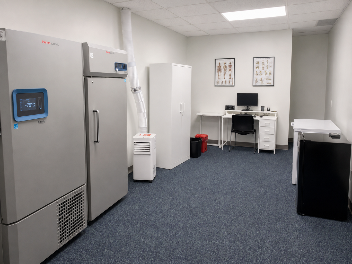 A medical laboratory with scientific equipment, a computer desk, and anatomical posters on the wall.