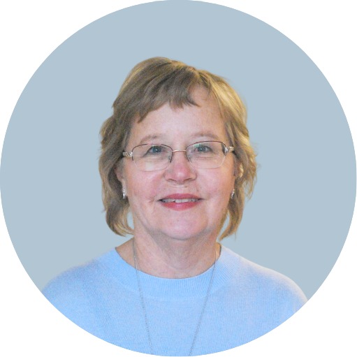 A smiling middle-aged woman with short light brown hair, glasses, and earrings, wearing a light blue shirt, against a teal background.