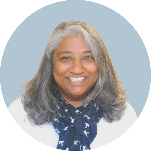 Smiling woman with shoulder-length gray hair, wearing a white top and navy scarf with white bird patterns, against a light teal circular background.