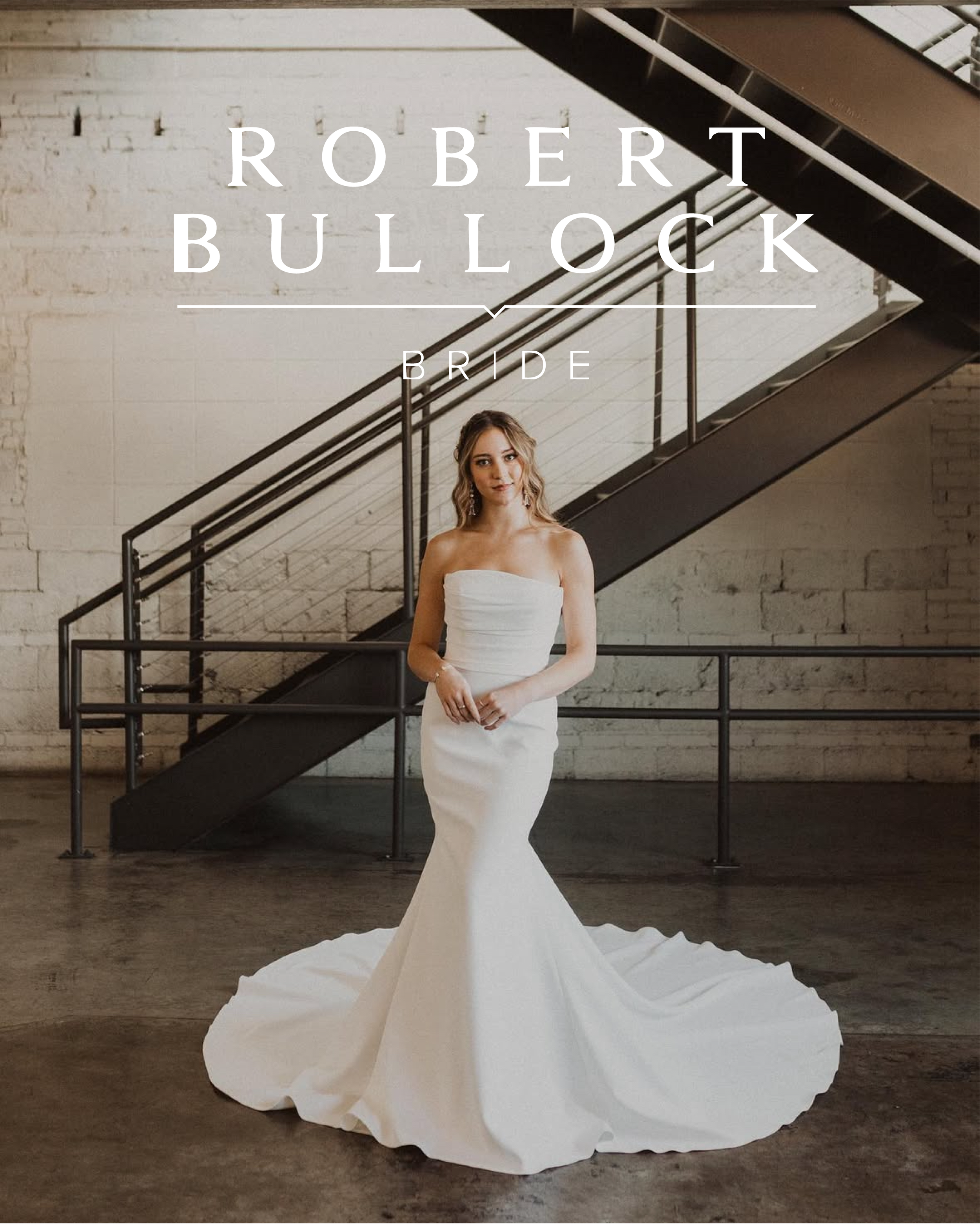 A woman in a strapless white wedding dress standing in an industrial-style space with brick walls and a black metal staircase behind her.