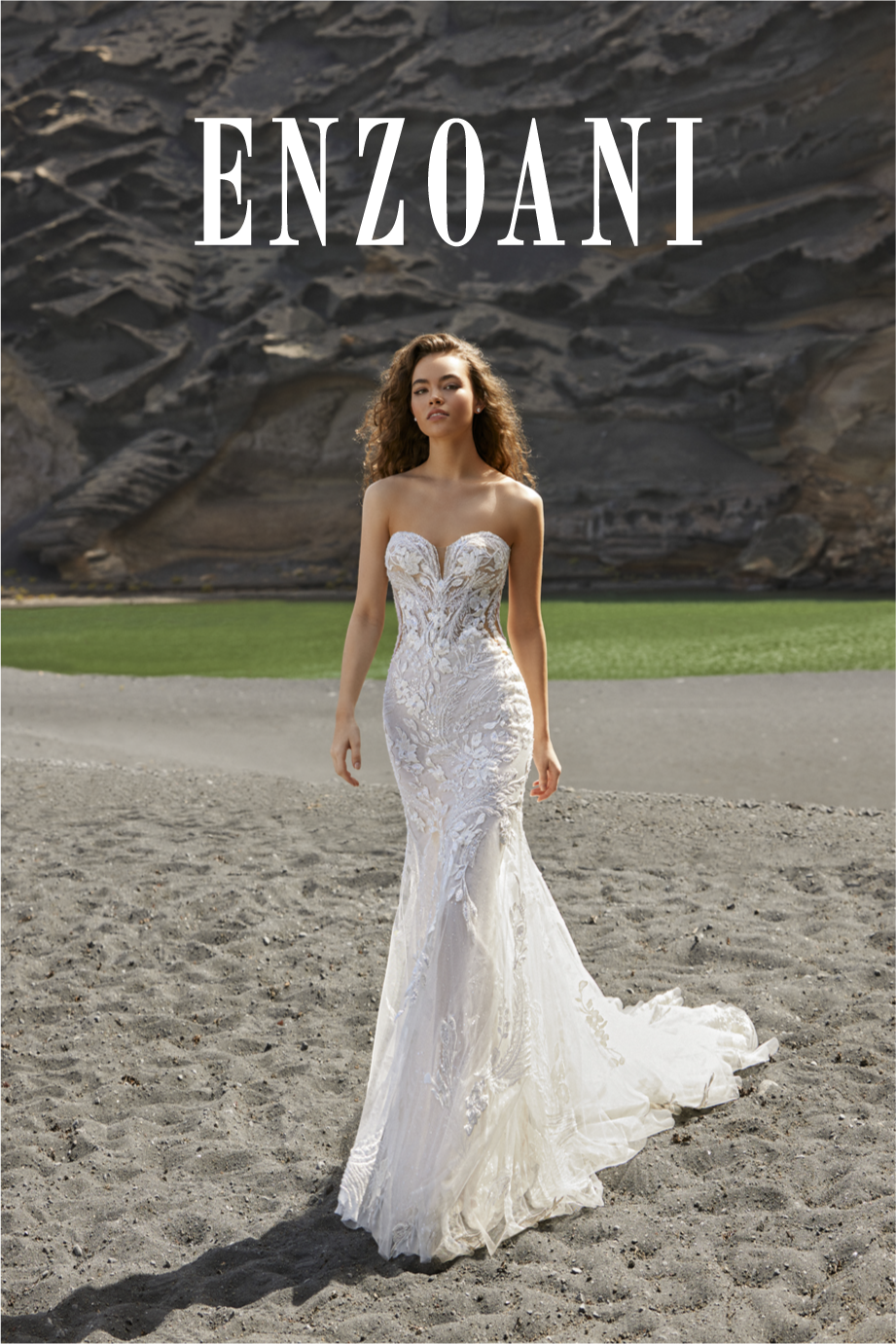 A woman in a strapless, white lace wedding gown walking on the sandy beach with rocky cliffs in the background and the word "ENZOANI" at the top.