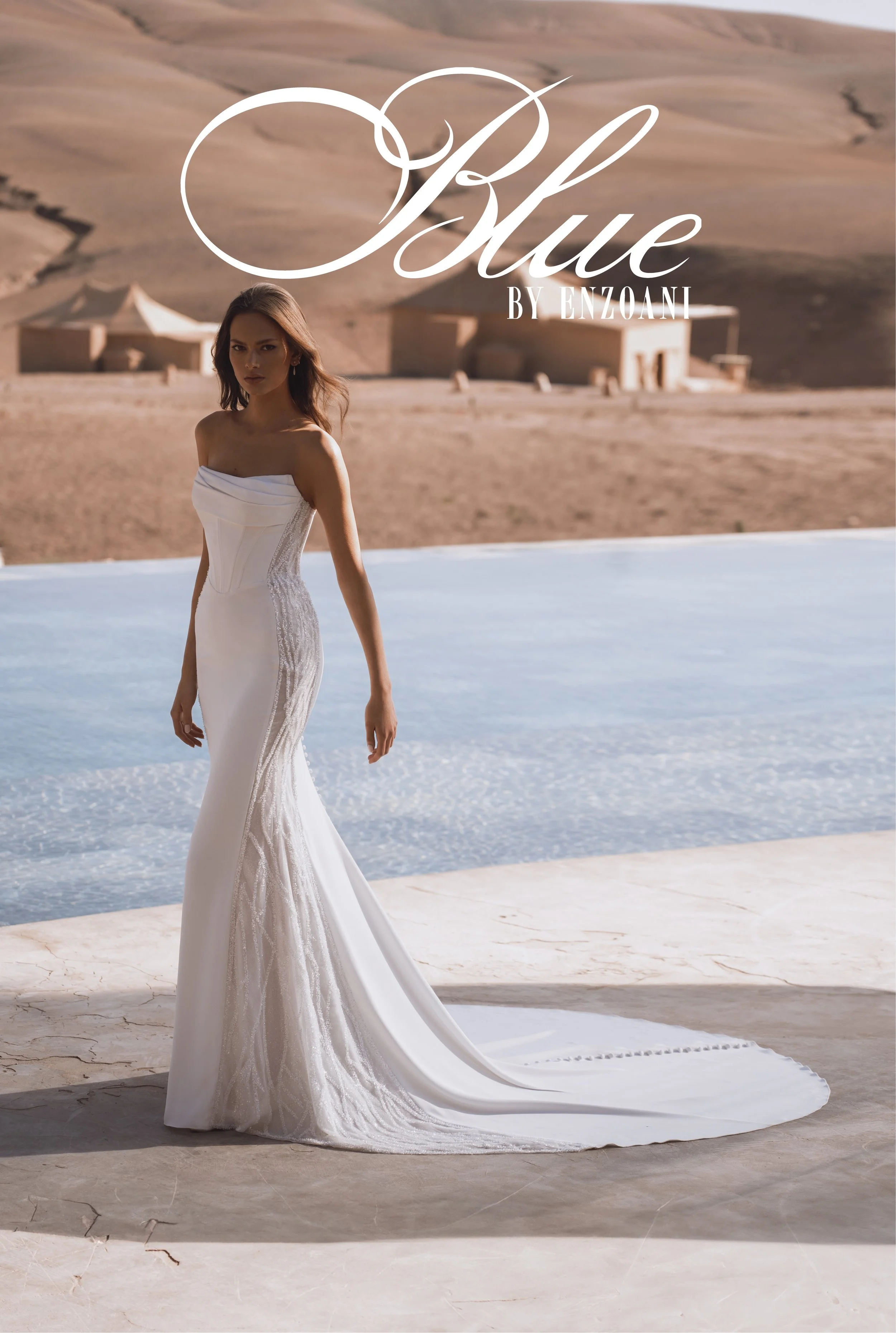 Woman in a white strapless wedding dress standing outdoors near a pool with desert landscape in the background