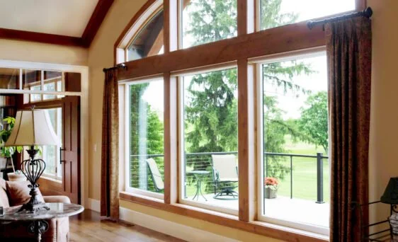 Living room with large bay windows looking out to a green backyard with a balcony and outdoor furniture.