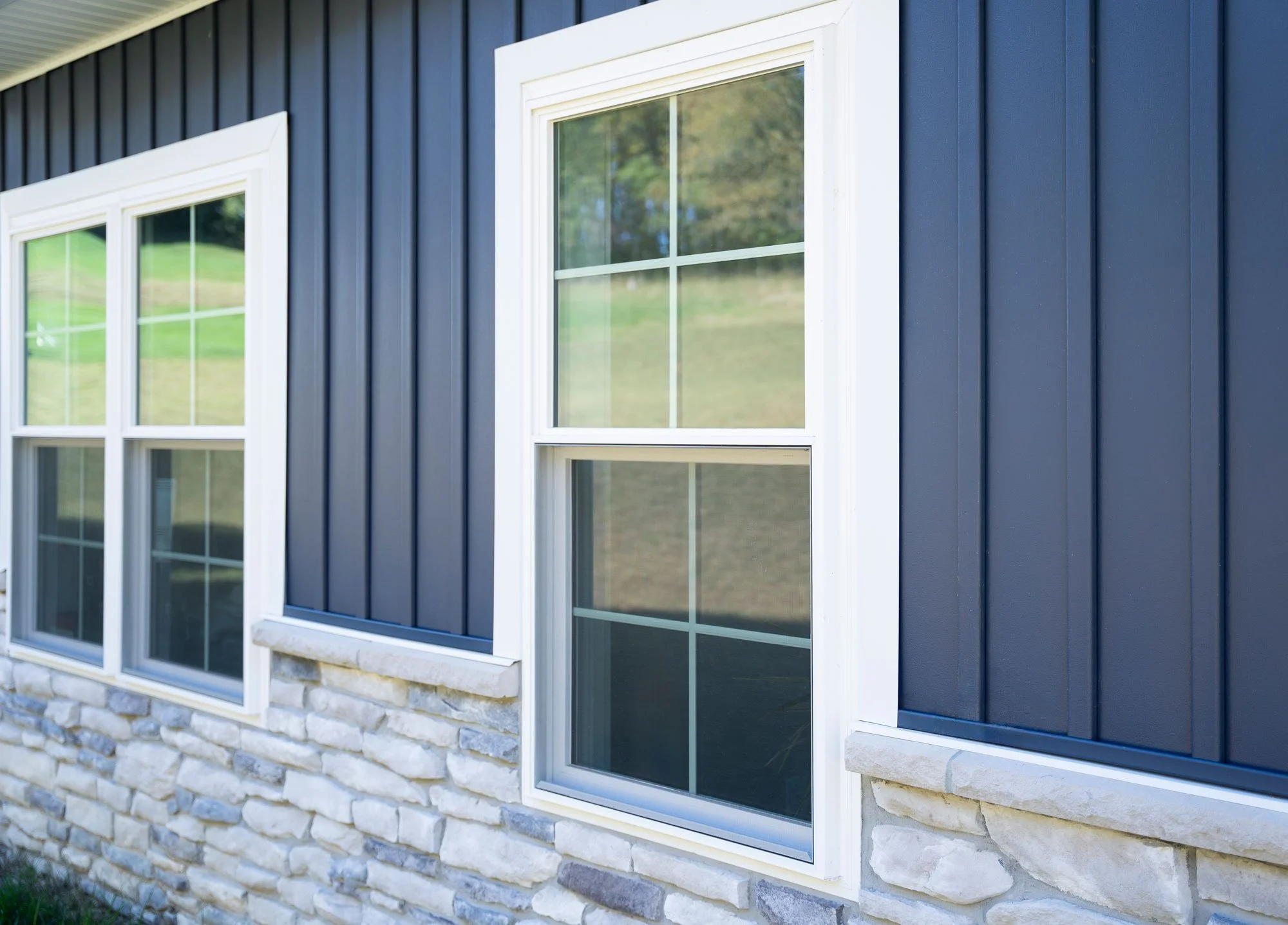 Close-up of the exterior wall of a house showing blue siding, white window frames, and a stone foundation.