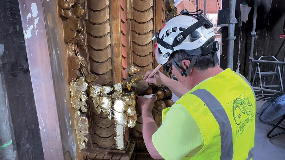 A conservationist adds gold leaf gilding to the cleaned and patched proscenium.