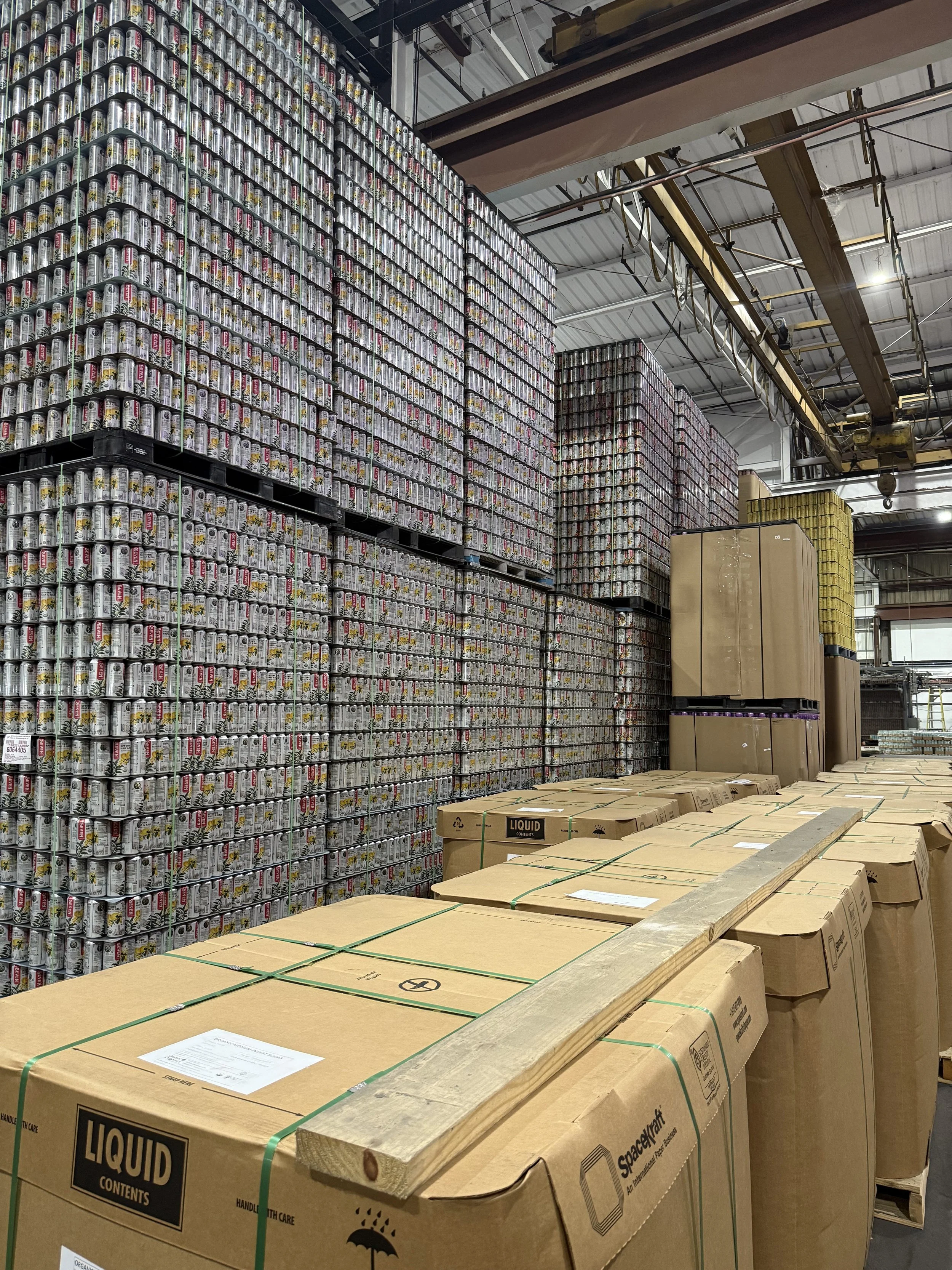 Stacks of canned beverages and large boxes in a warehouse setting.