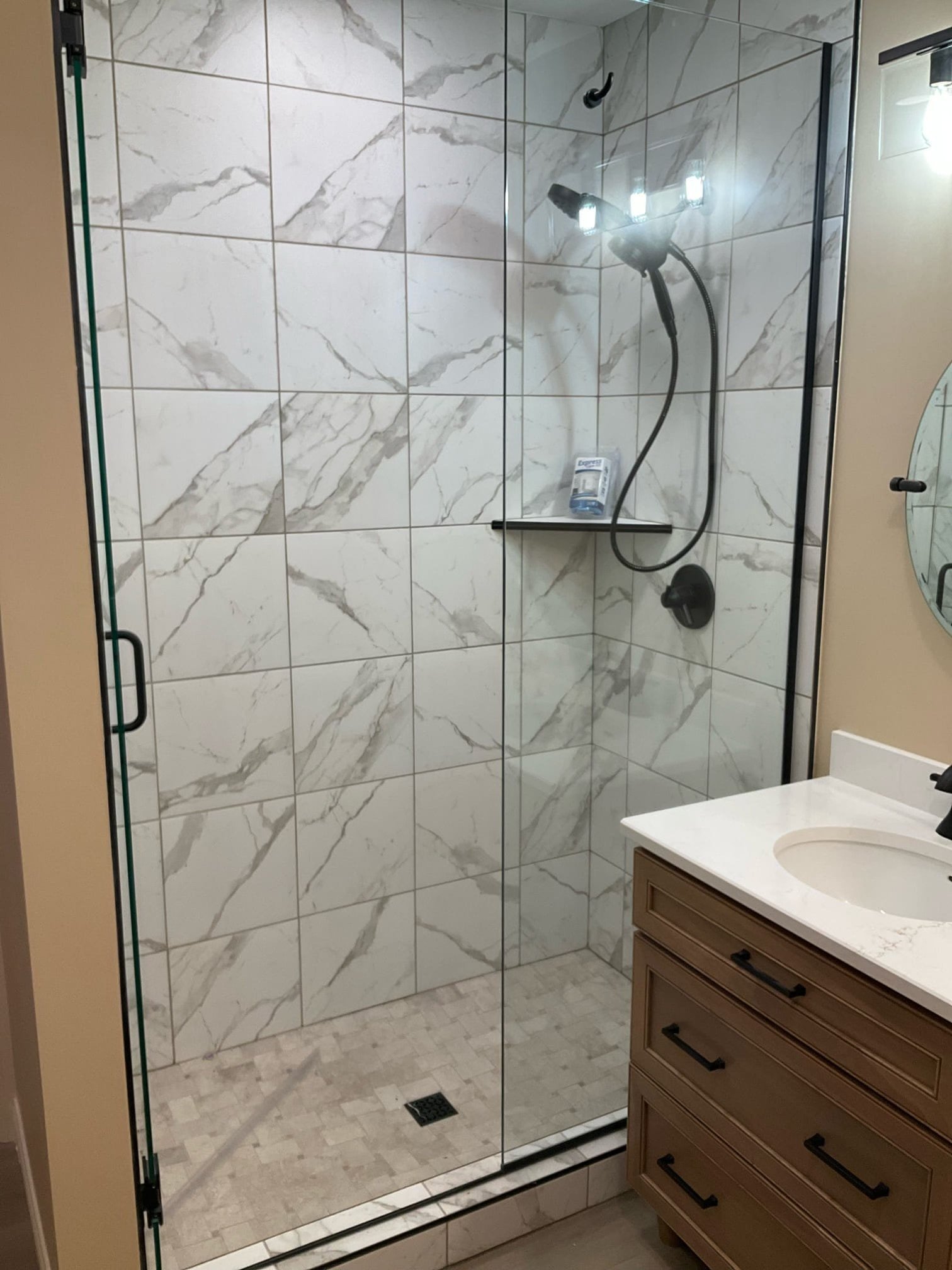 Frameless glass shower with large-format marble-look tiles and matte black hardware.