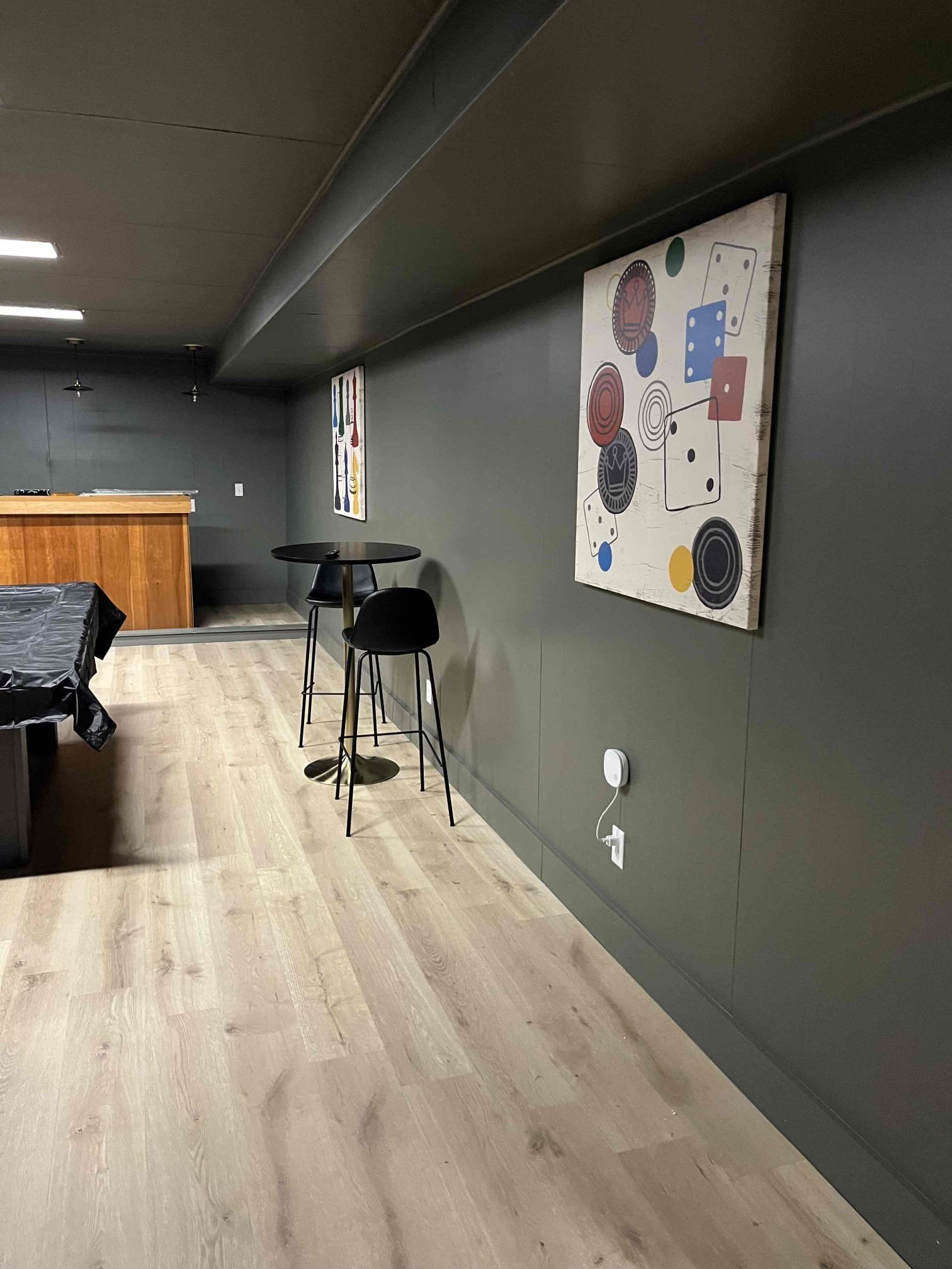 Modern basement bar and game area with painted walls, custom artwork, pub-style seating, and luxury vinyl plank flooring.