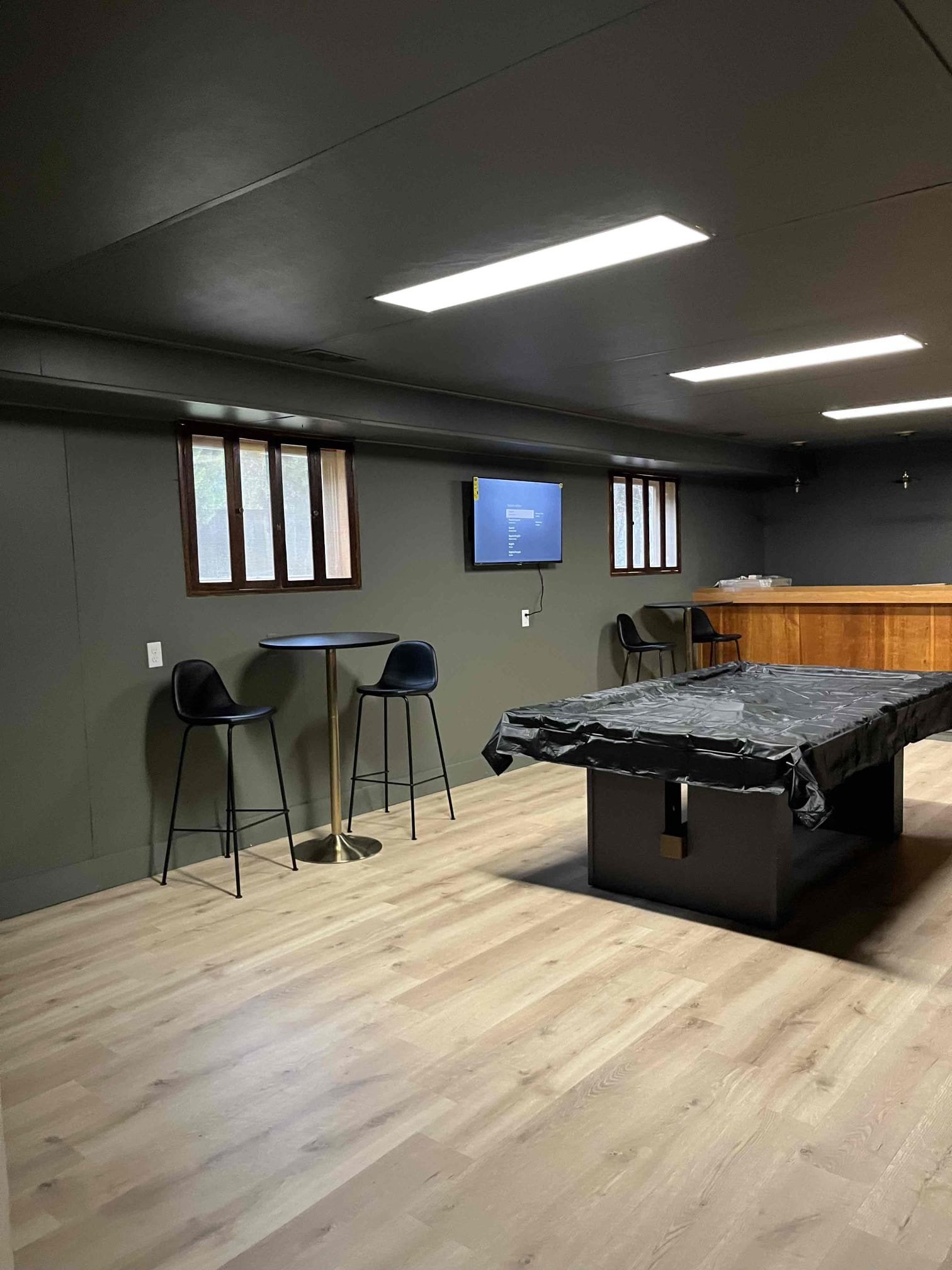 Remodeled basement recreation room with a pool table, bar area, and wall-mounted TV under sleek lighting and wood-style flooring.