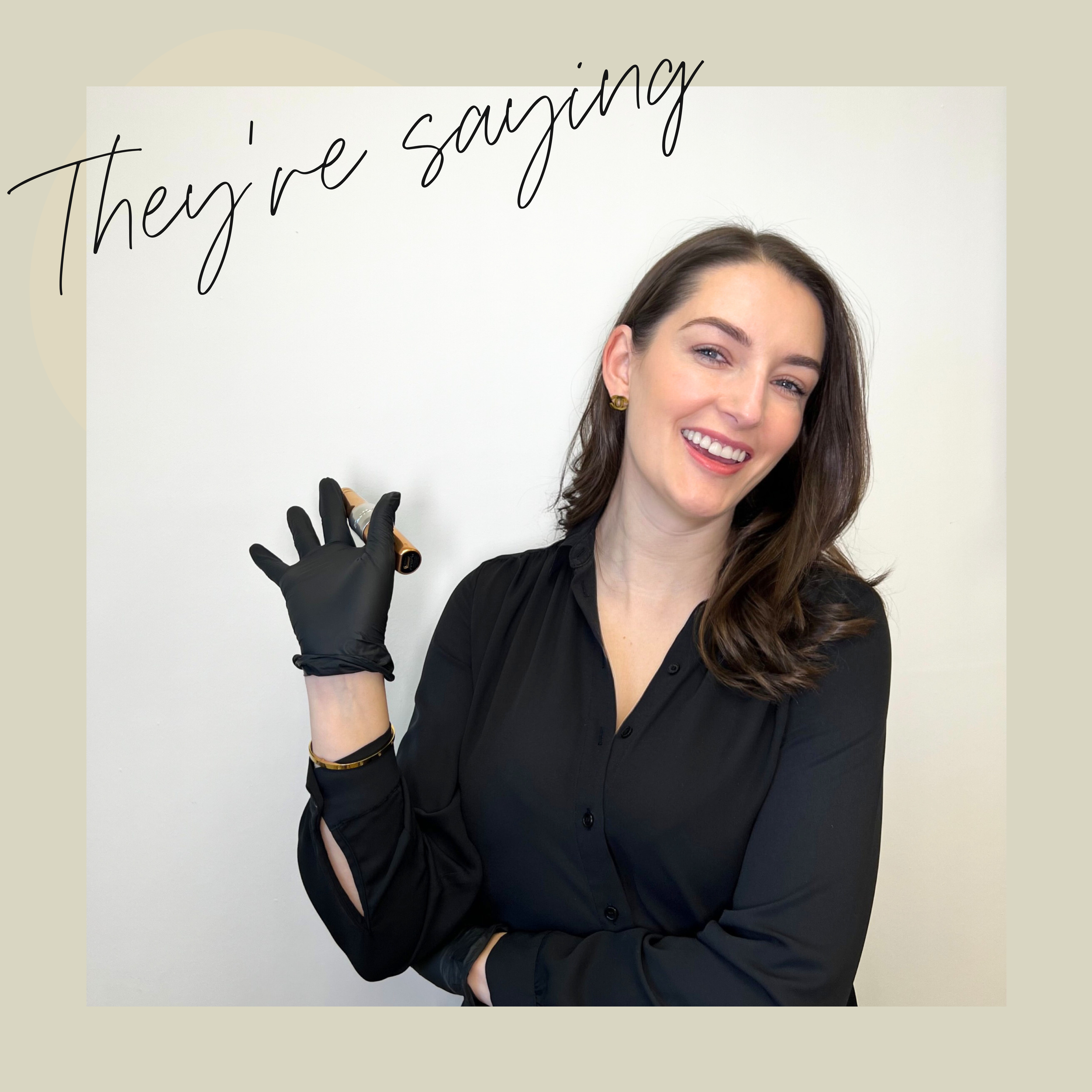 A woman with brown hair smiling and wearing a black blouse, holding a marker near her shoulder, standing in front of a whiteboard with the words 'They're saying' written in cursive.