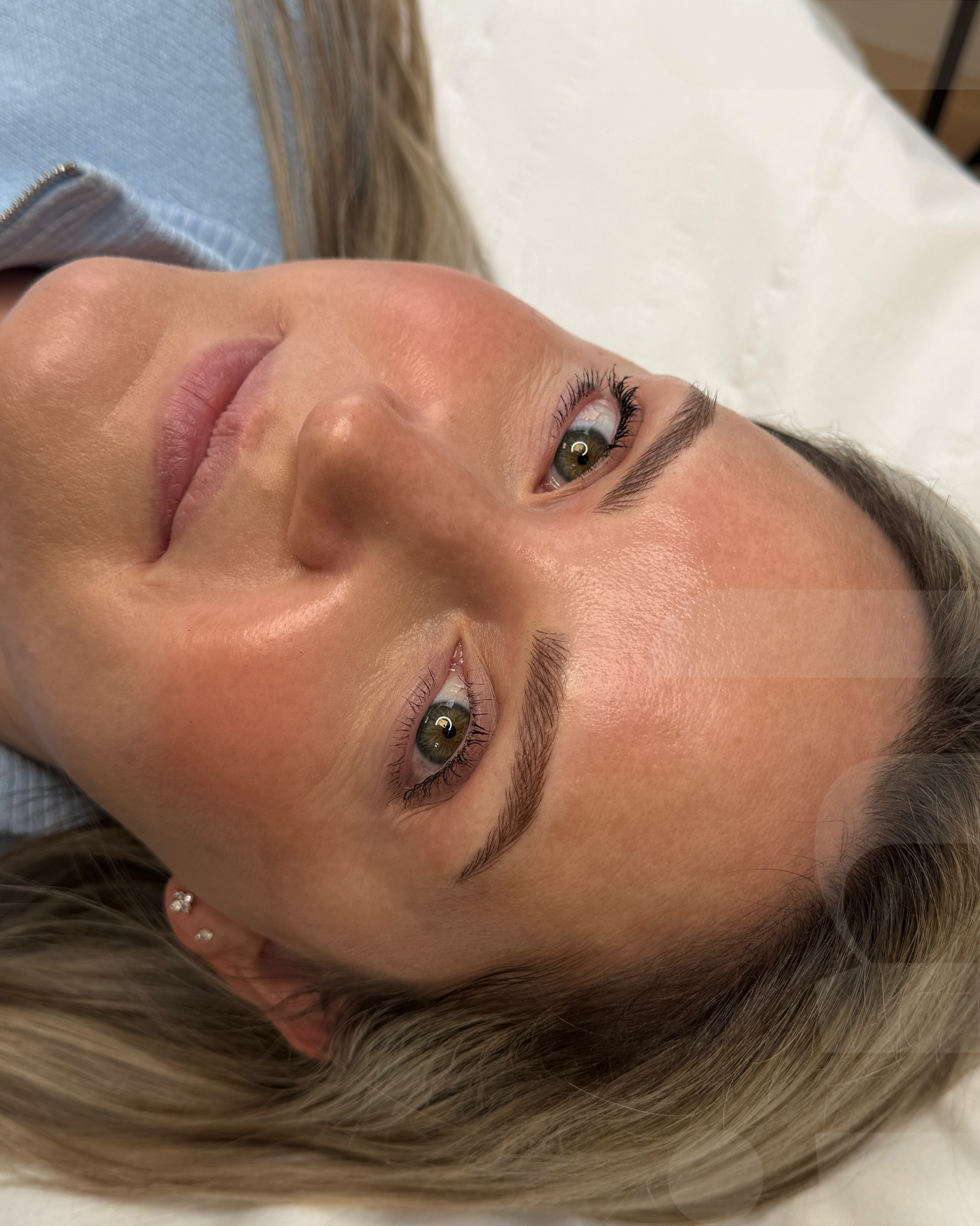 A woman lying down with her head turned to the side, showing her face with makeup and small earrings.