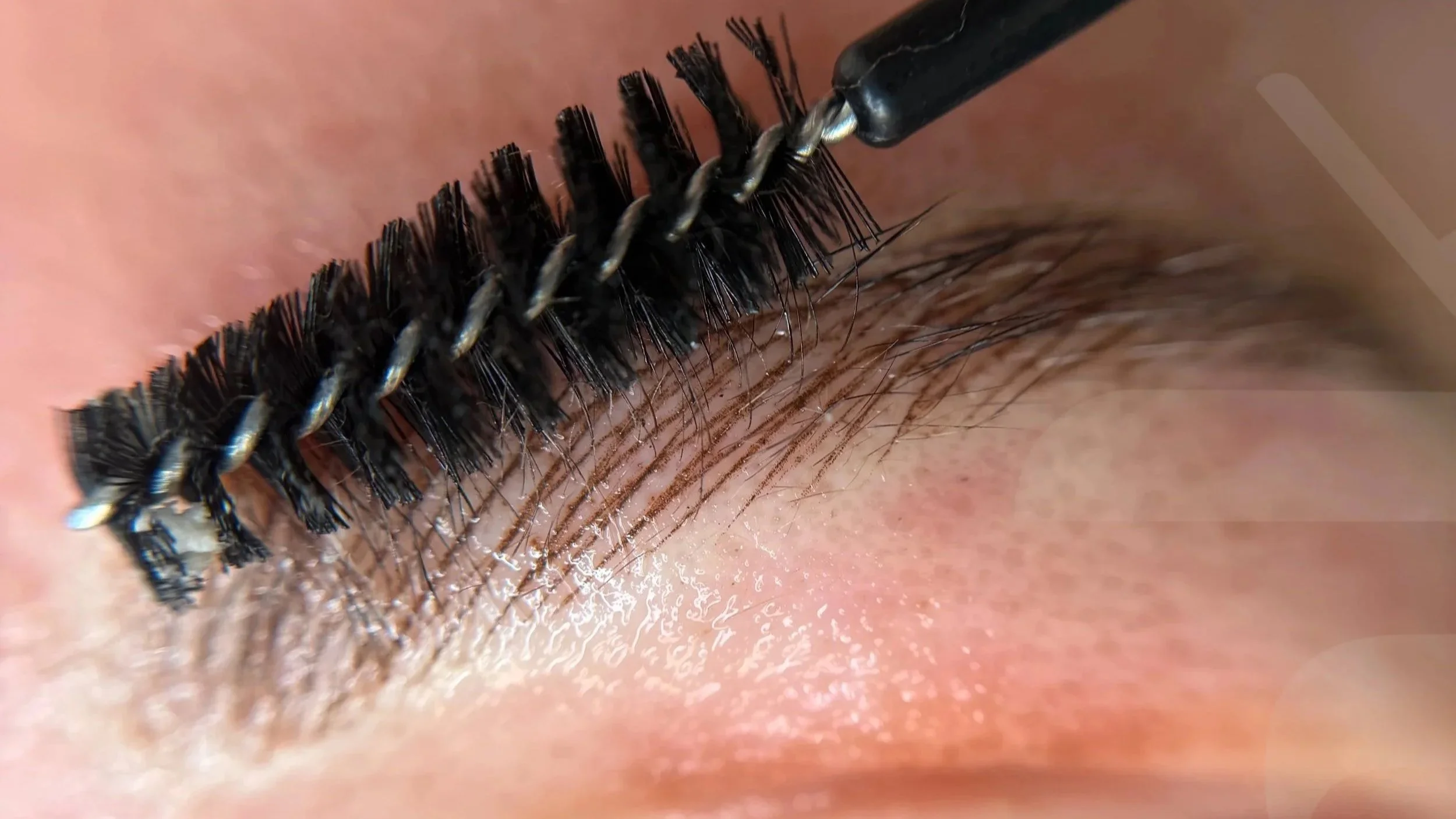 Close-up of a person applying mascara to eyelashes with a mascara wand.
