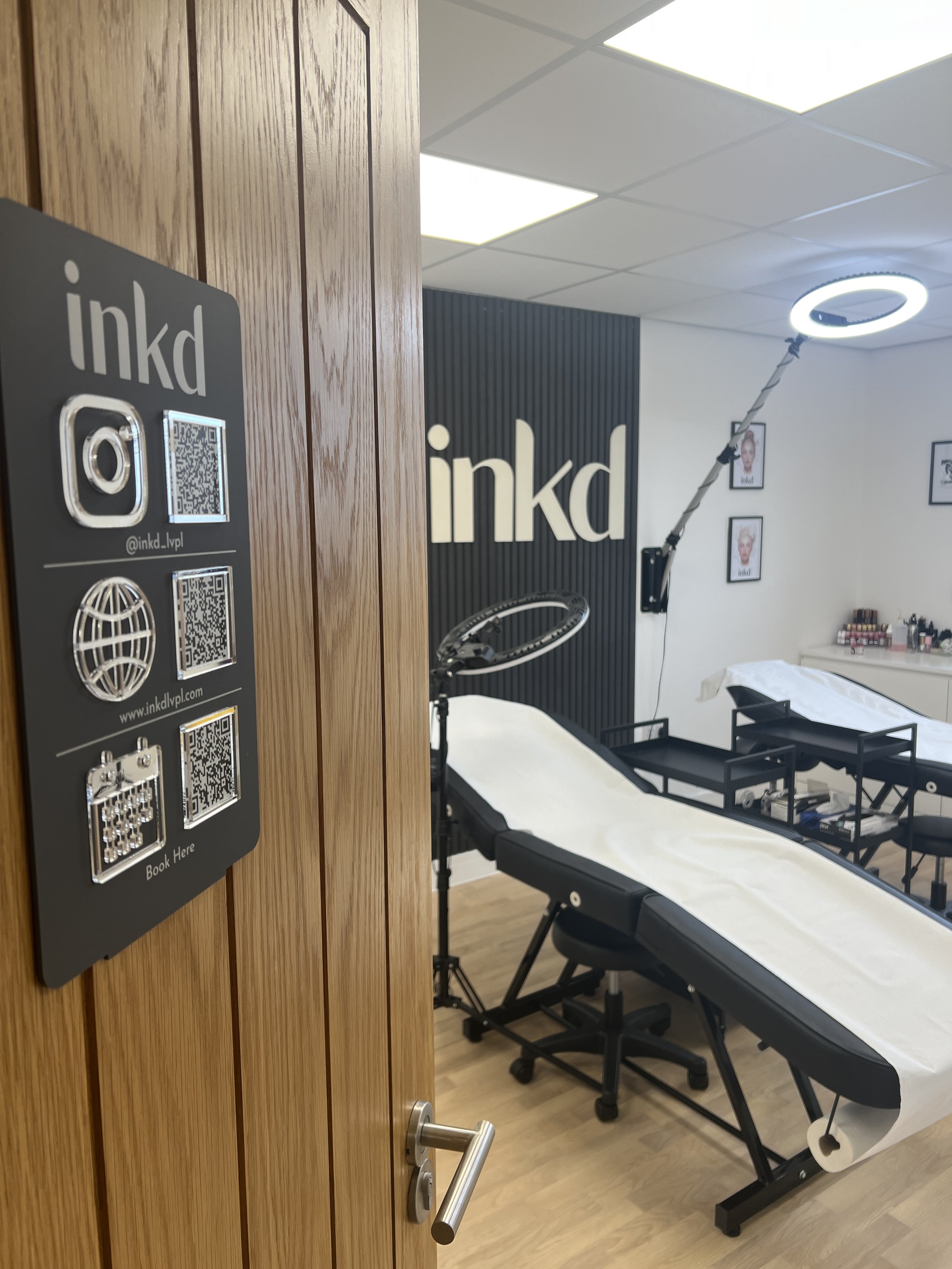 Interior of a tattoo parlor with tattoo beds, wall art, and a sign with the word 'inkd' on the wall.