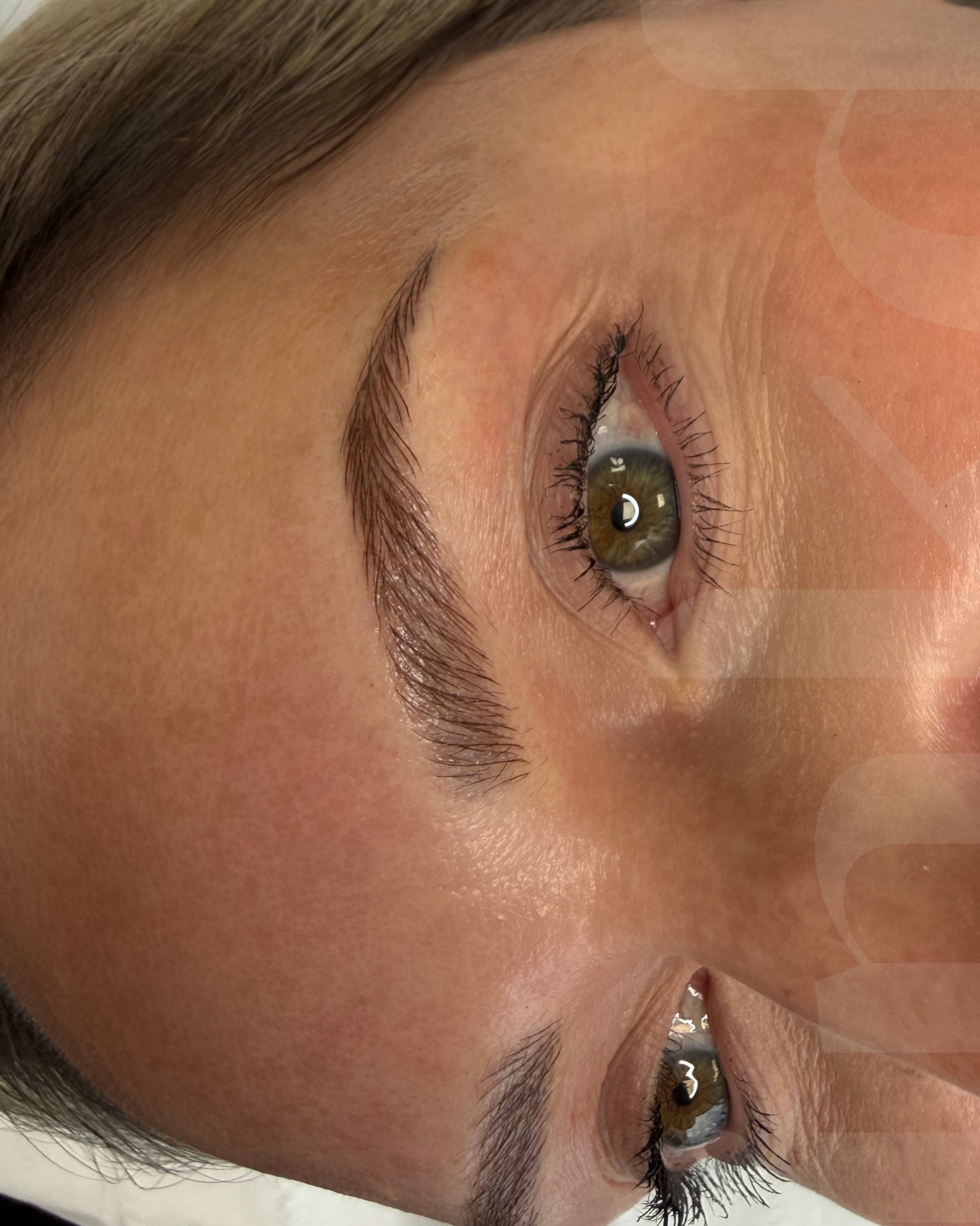 Close-up of a woman's face tilted sideways, focusing on her brown eyes with long eyelashes, eyebrows, and smooth skin.