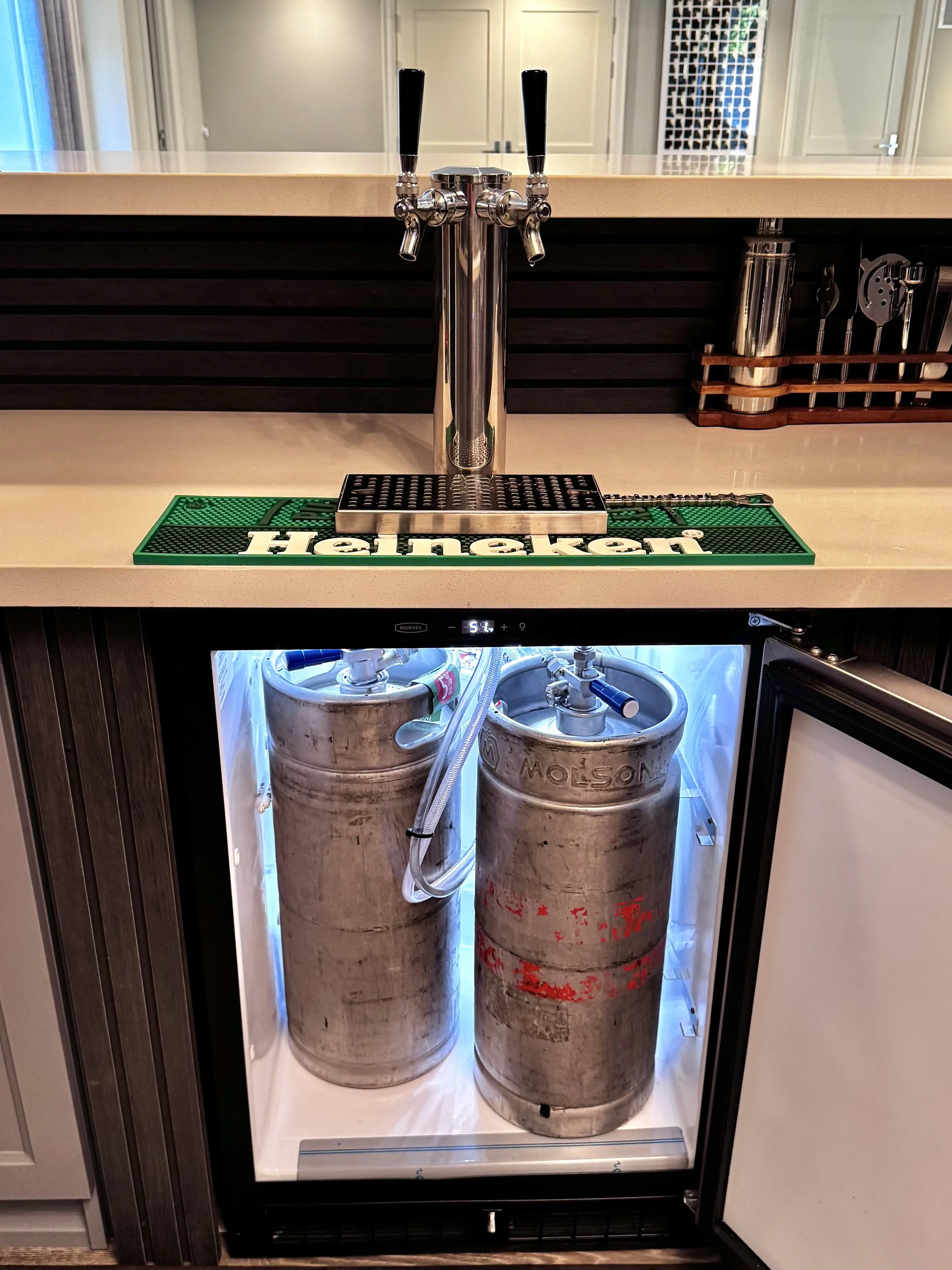 A bar area with a beer tap dispensing station on top of a mini fridge containing two large gas tanks.