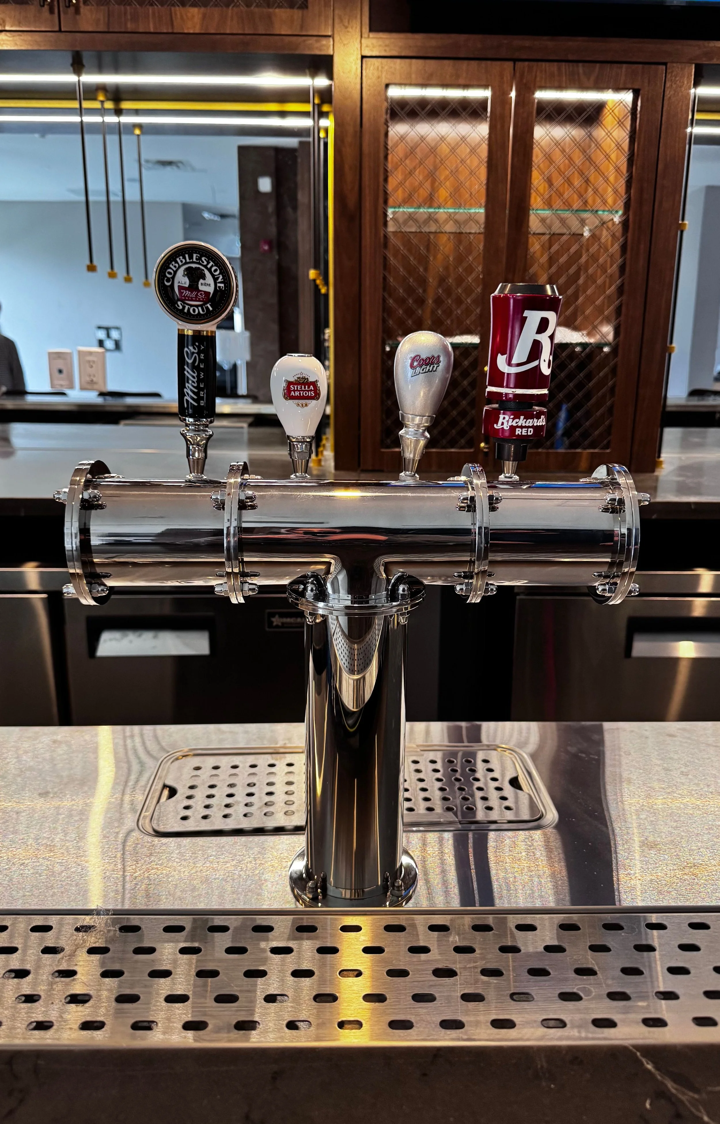 A bar with four beer taps, featuring labels for Cobblestone Stout, Stella Artois, Coors Light, and Blackened Red.