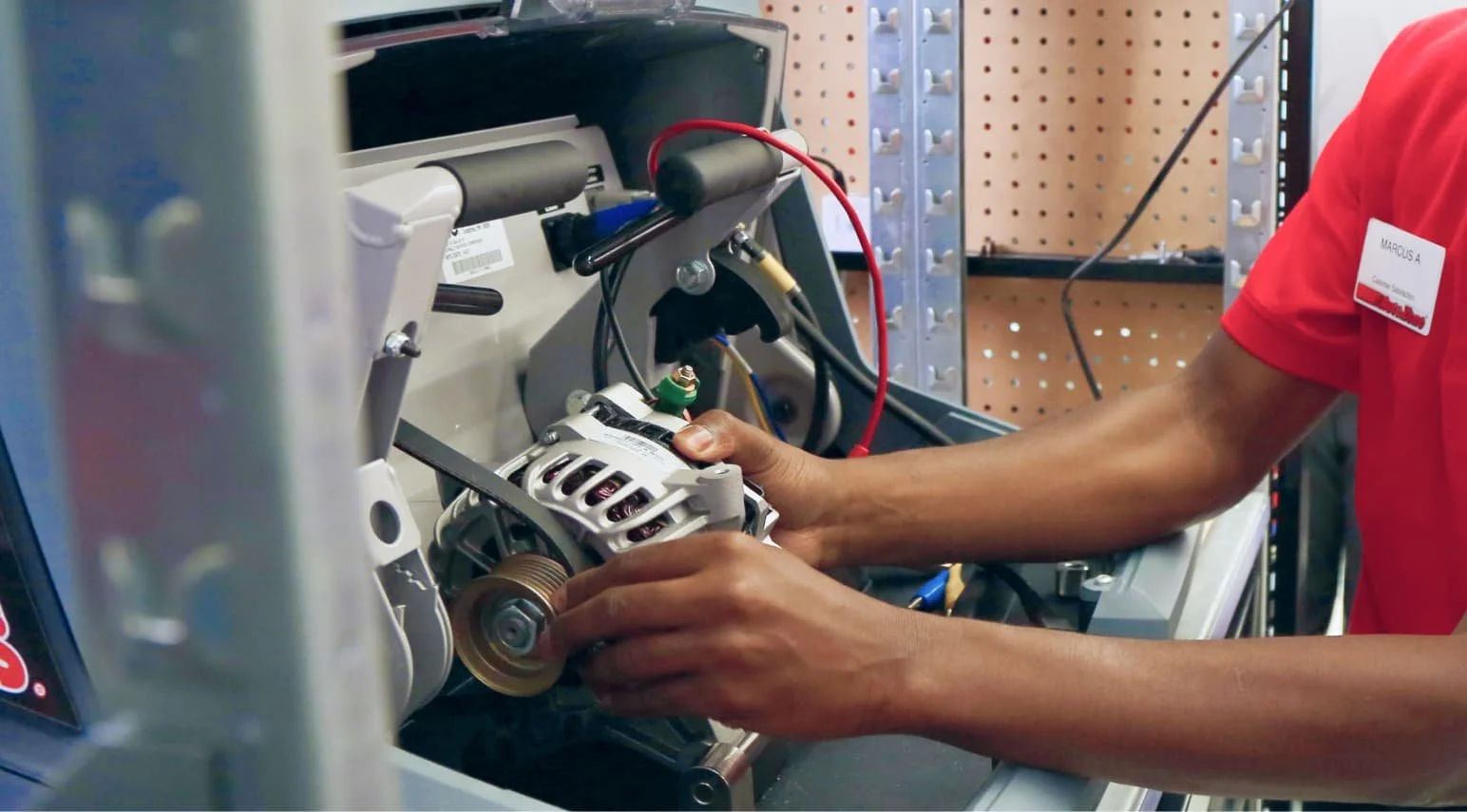 A technician wearing a red shirt is assembling or repairing an electrical or electronic device with wires and components inside a metal enclosure, possibly a piece of testing or medical equipment.