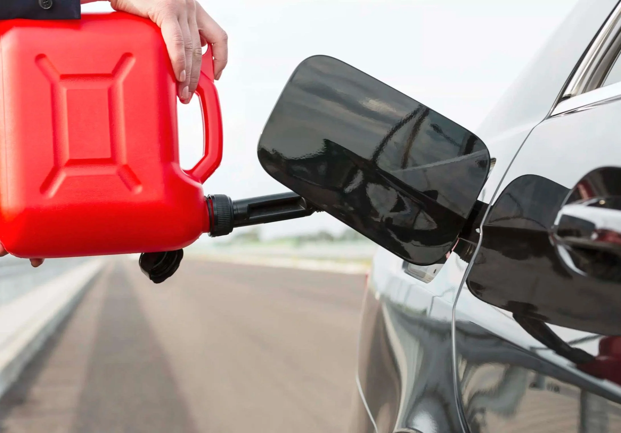 A person refueling a black car at a gas station using a red gasoline container.