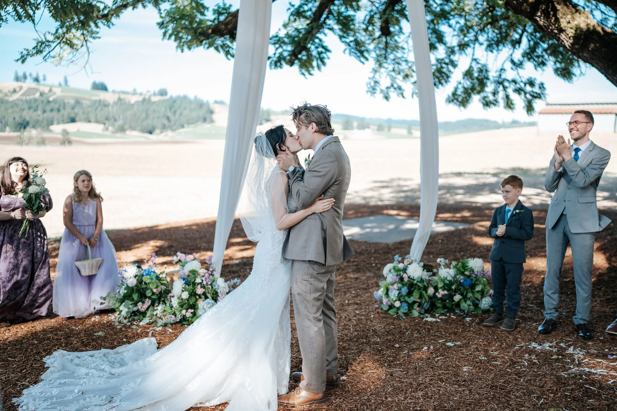 Romantic first kiss during an outdoor wedding ceremony in Humboldt County. Bride and groom share an intimate moment at their Northern California celebration. Photo by Tex Kelly Photography.