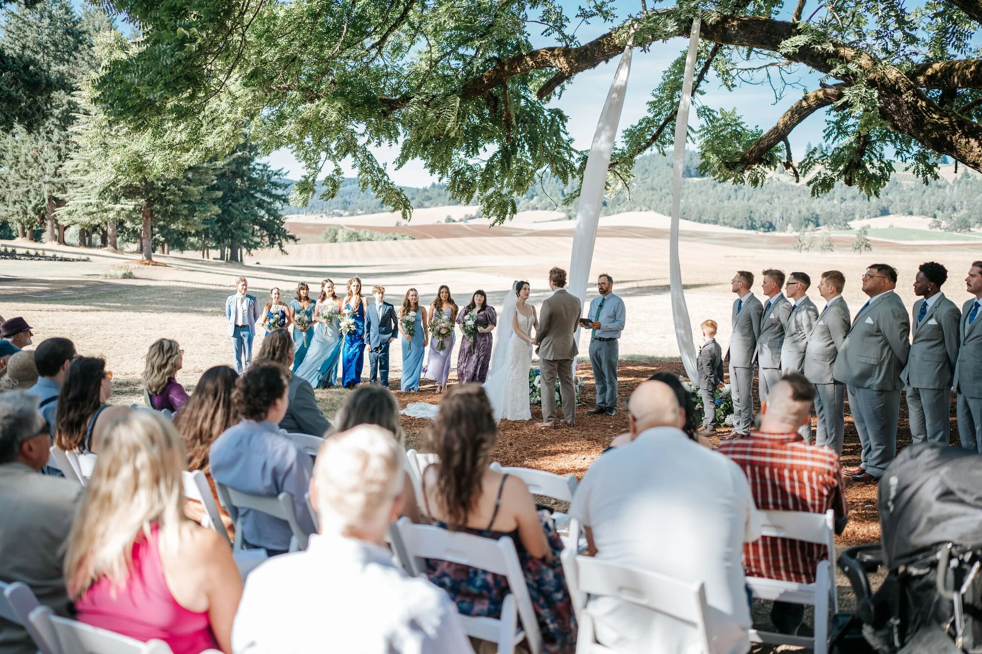 Outdoor wedding ceremony under a beautiful oak tree in Humboldt County, California. Guests watch as the bride and groom exchange vows at this rustic Northern California venue. Wedding photography by Tex Kelly Photography.