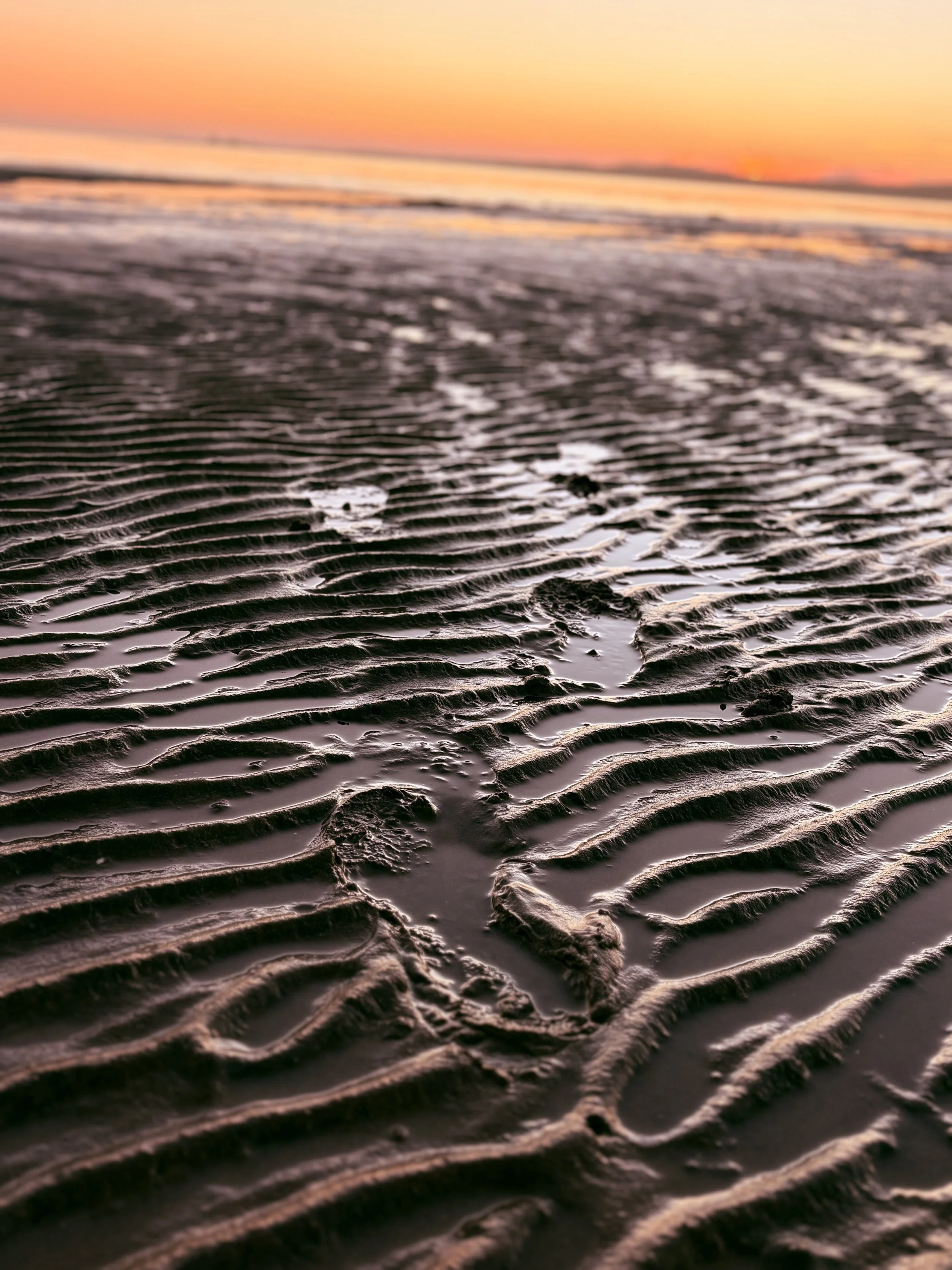 Close-up of rippled sand on a beach with footprints, with a sunset sky in the background