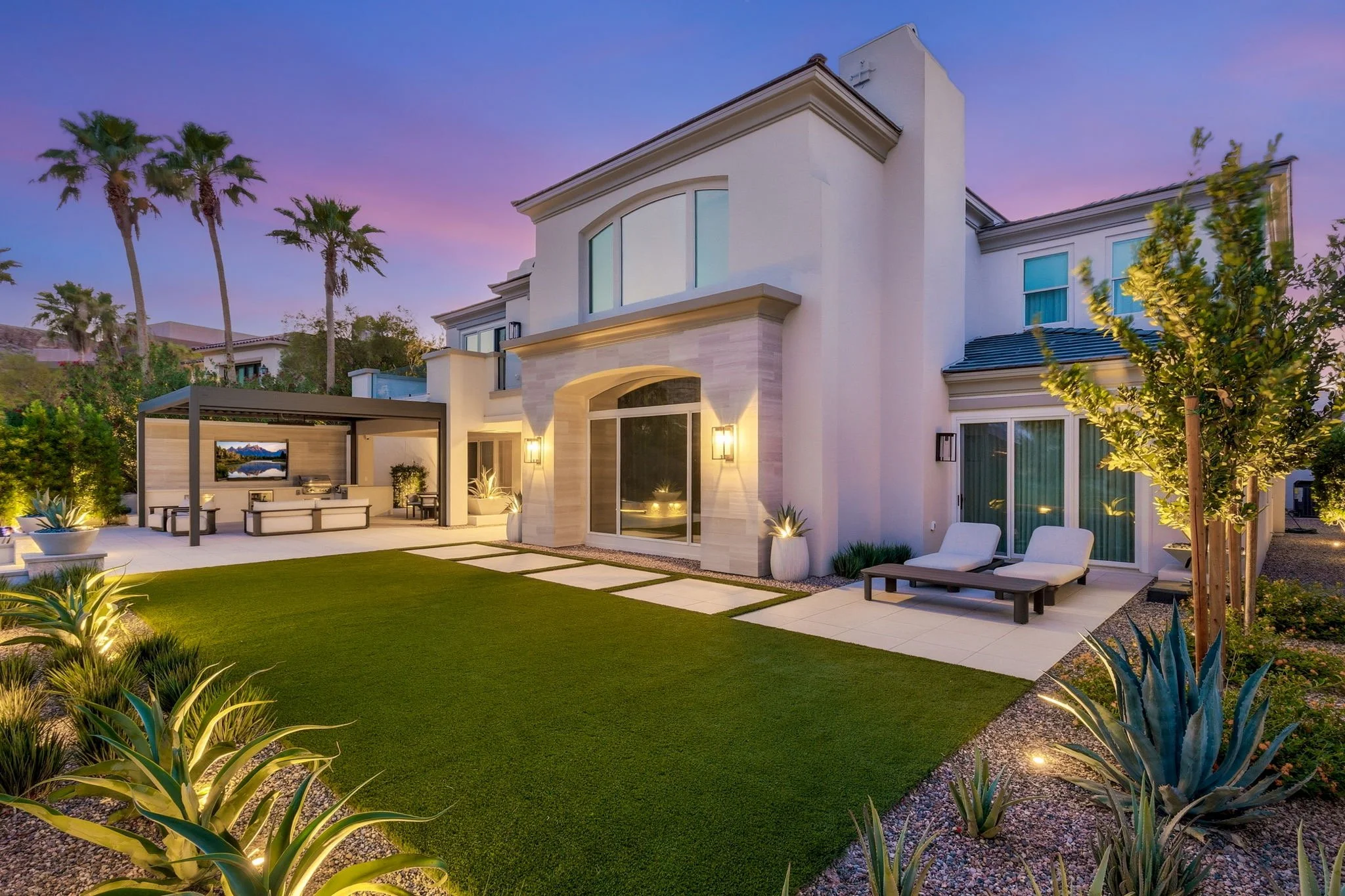 landscape design with manicured green lawn, palm trees, and dusk exterior lighting on Morning Grove Dr, Las Vegas.