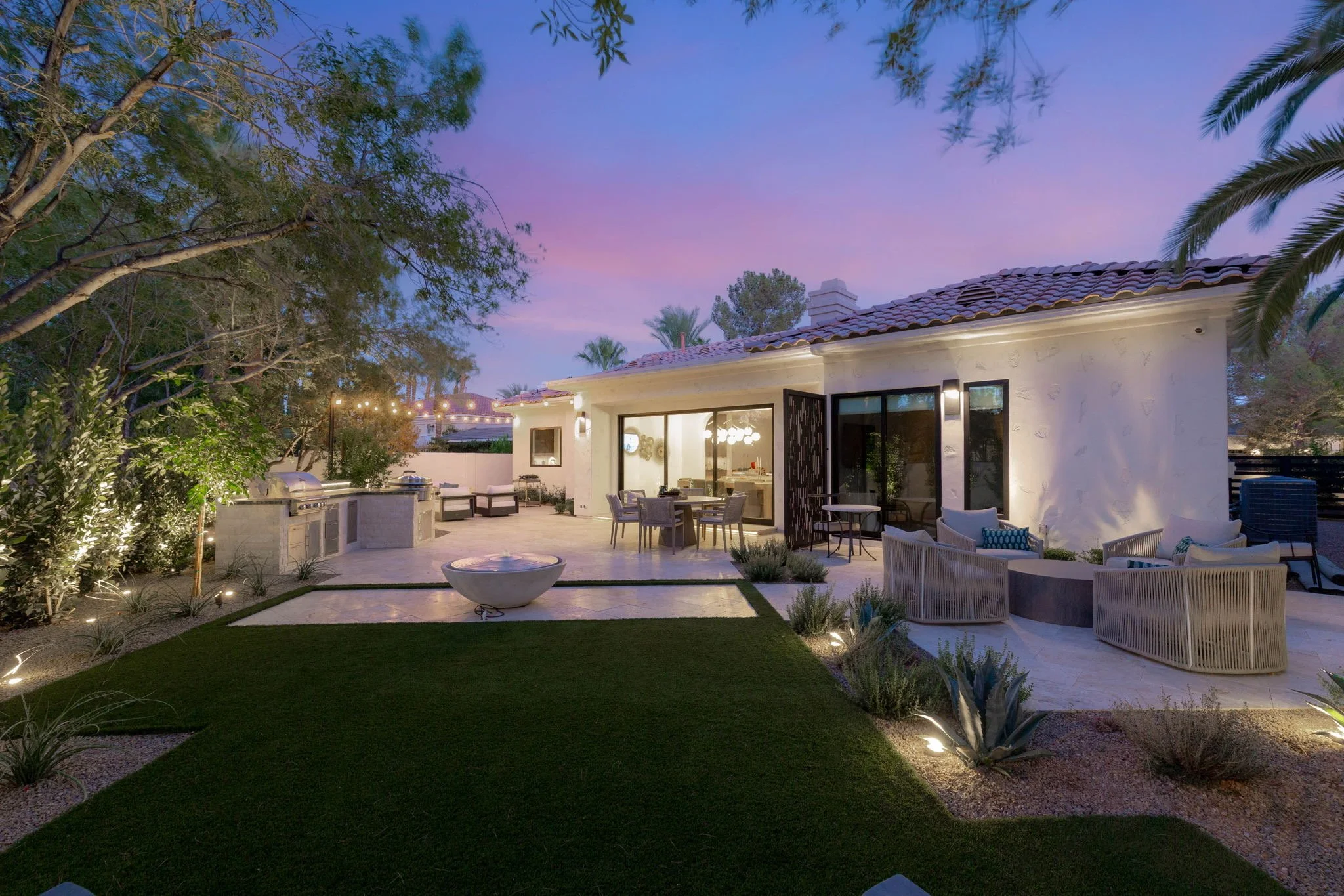 Custom backyard pool installation with raised jacuzzi, synthetic turf, and illuminated stone retaining wall in Las Vegas.