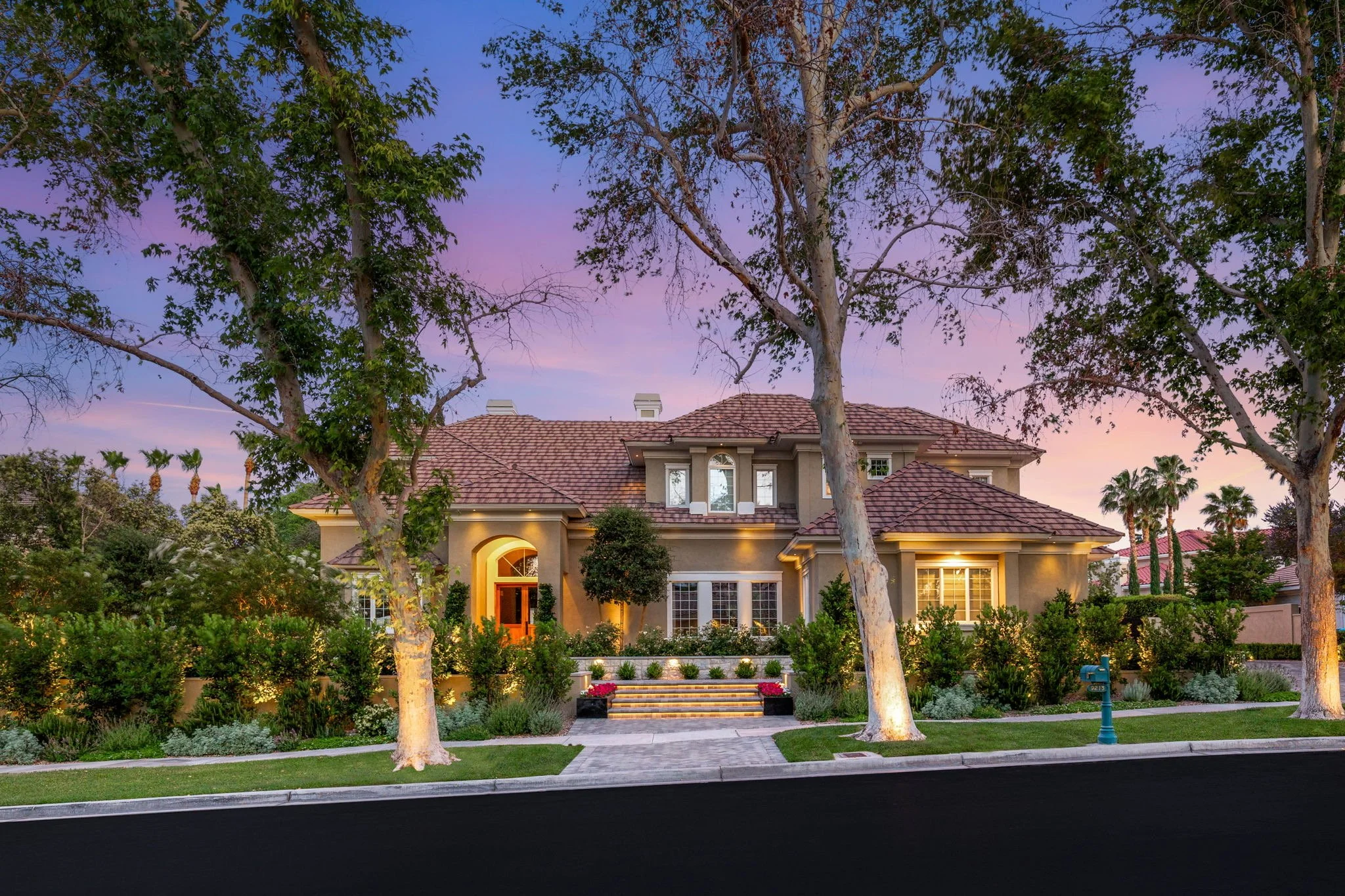 Custom front yard curb appeal landscaping for a Mediterranean luxury estate featuring twilight tree uplighting and stone entryway steps in Las Vegas NV.