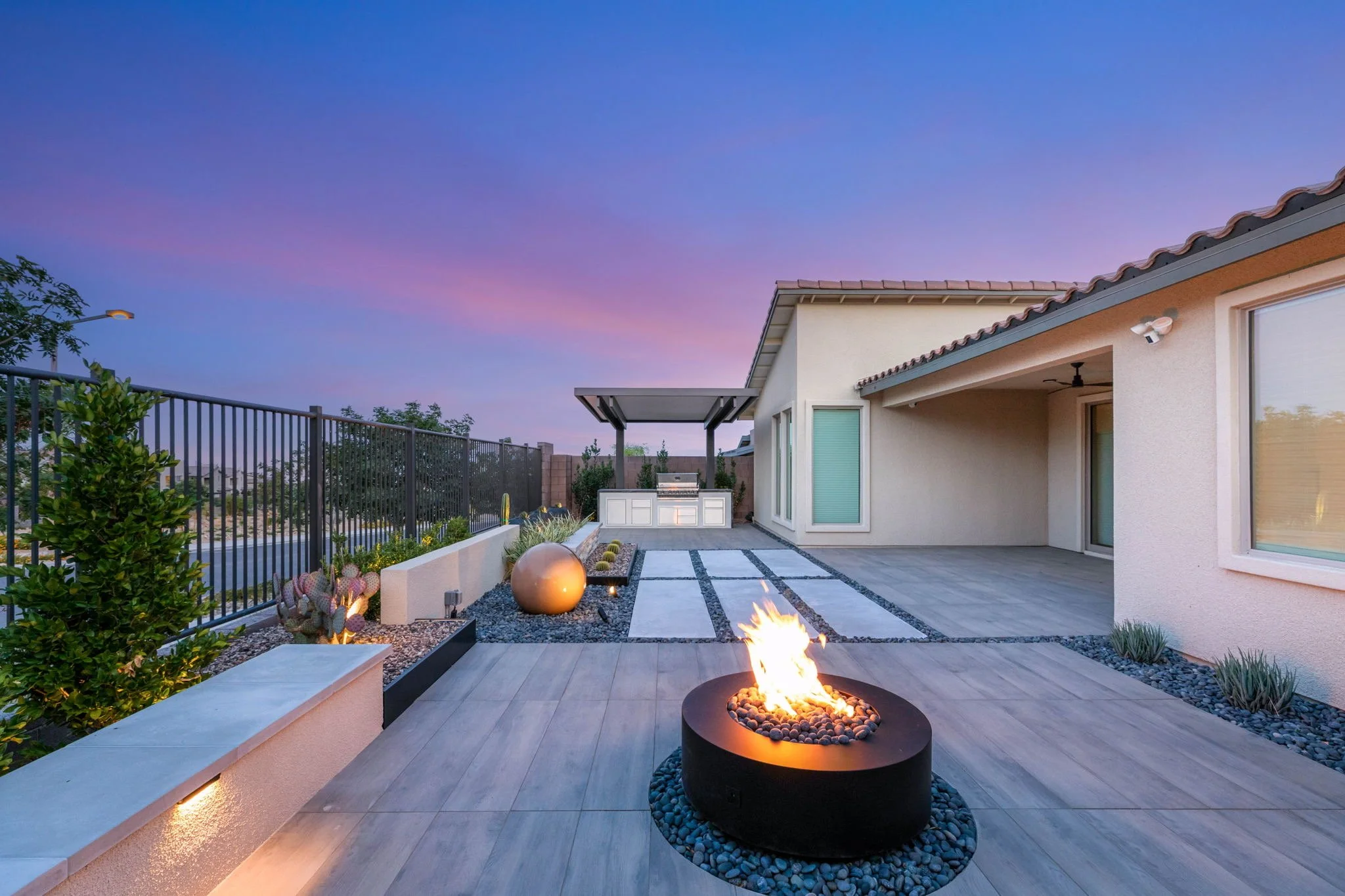 Custom backyard patio lounge featuring round outdoor fire pit, decorative paver striping, and dusk exterior lighting in Las Vegas NV.