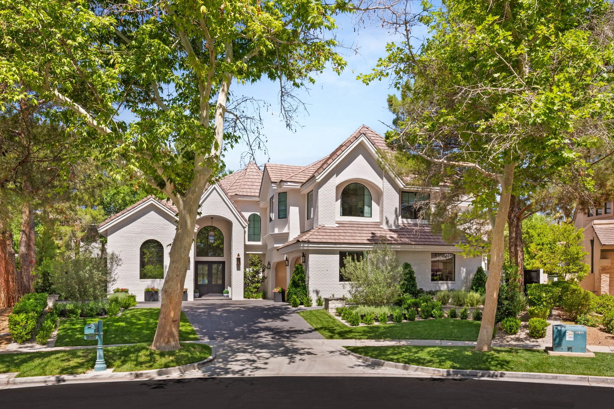 Custom front yard curb appeal landscaping for European-style luxury estate featuring white brick facade and lush garden beds in Las Vegas NV.