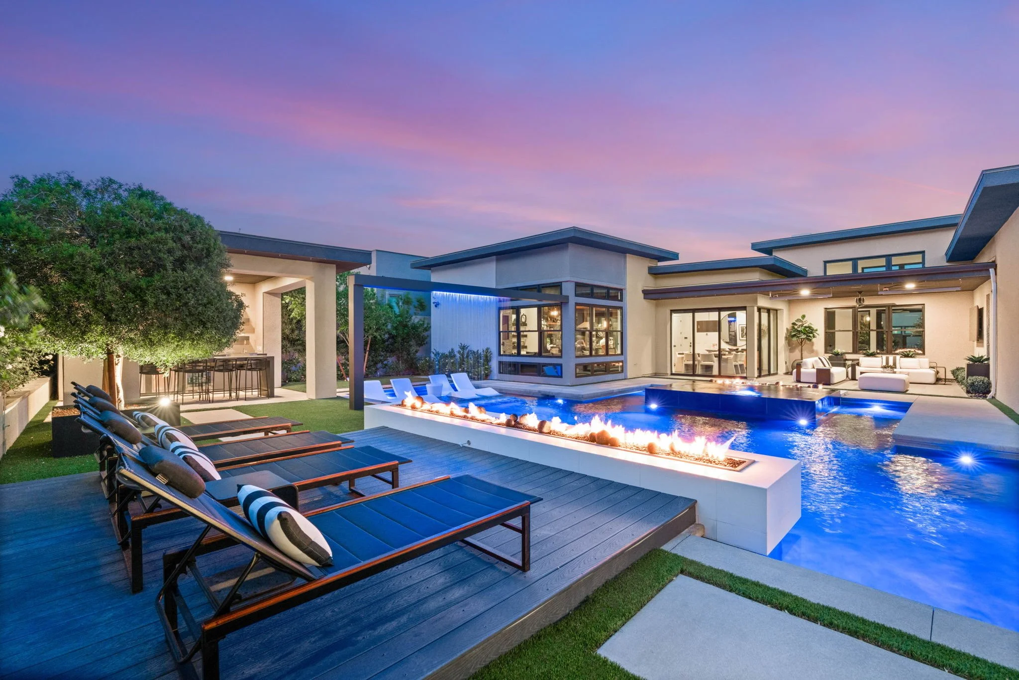 Custom luxury pool installation with integrated outdoor fire feature, poolside wood decking, and ambient twilight lighting in Las Vegas.